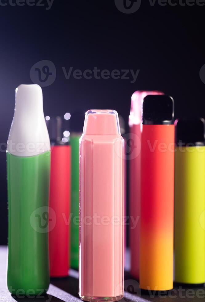A set of colorful disposable electronic cigarettes of different shapes on a black background with smoke. Concept of modern smoking, vaping and nicotine. photo