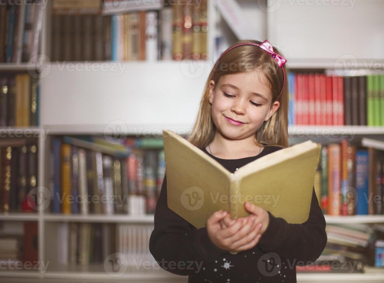 Cute little schoolgirl holding book and reading photo