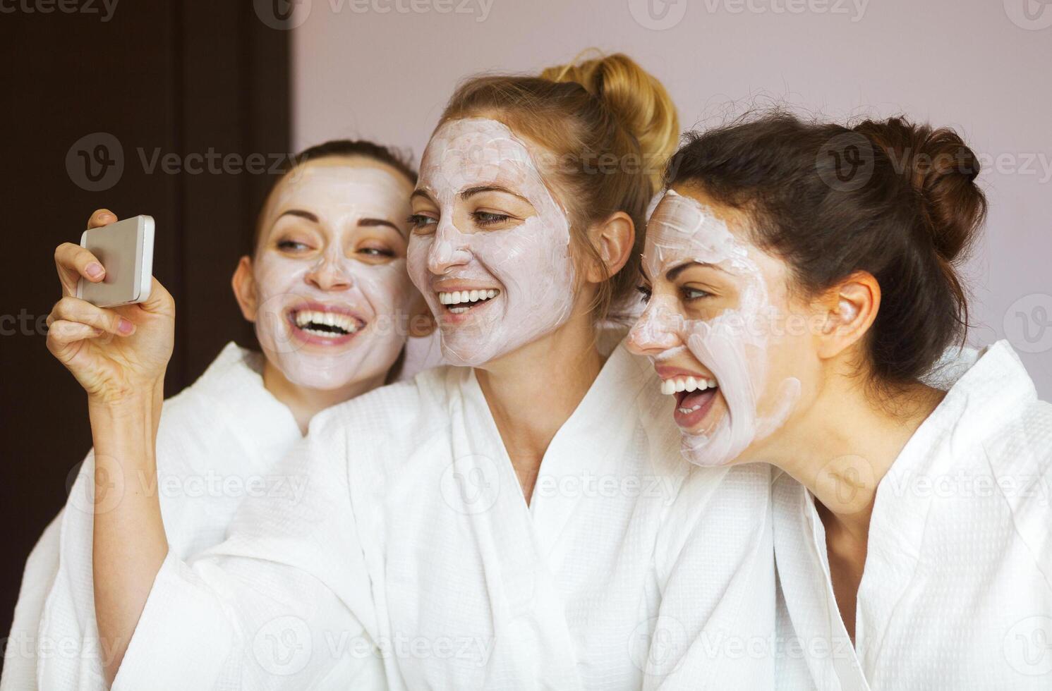 Three young happy women with face masks at spa resort. Frenship and wellbeing concept photo