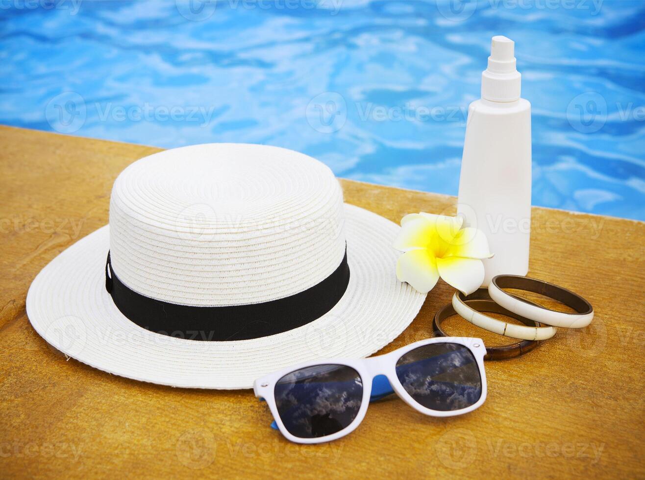 Suncream, sunglasses, hat, bracelet near the swimming pool photo