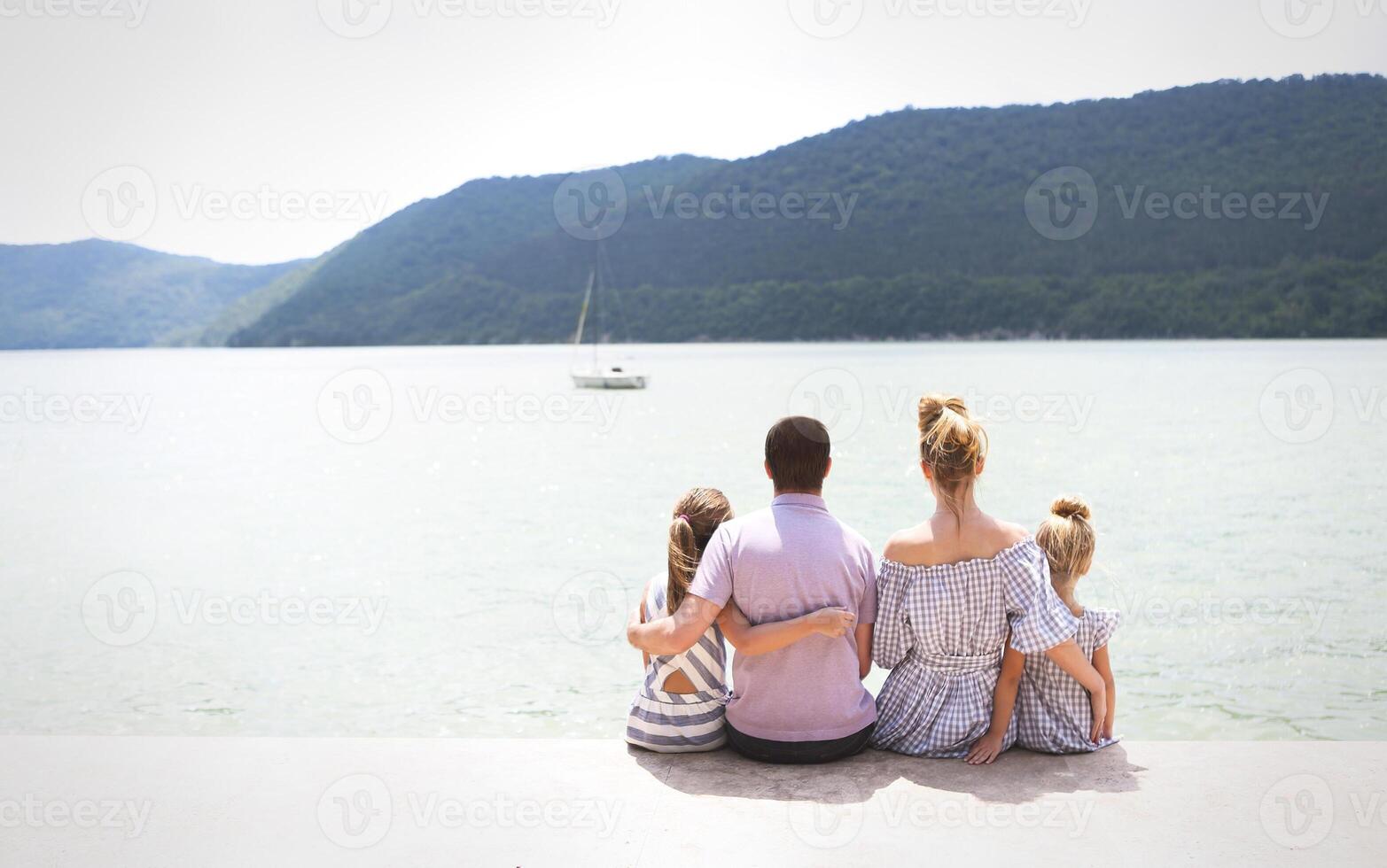 Young family of four sitting by lake photo