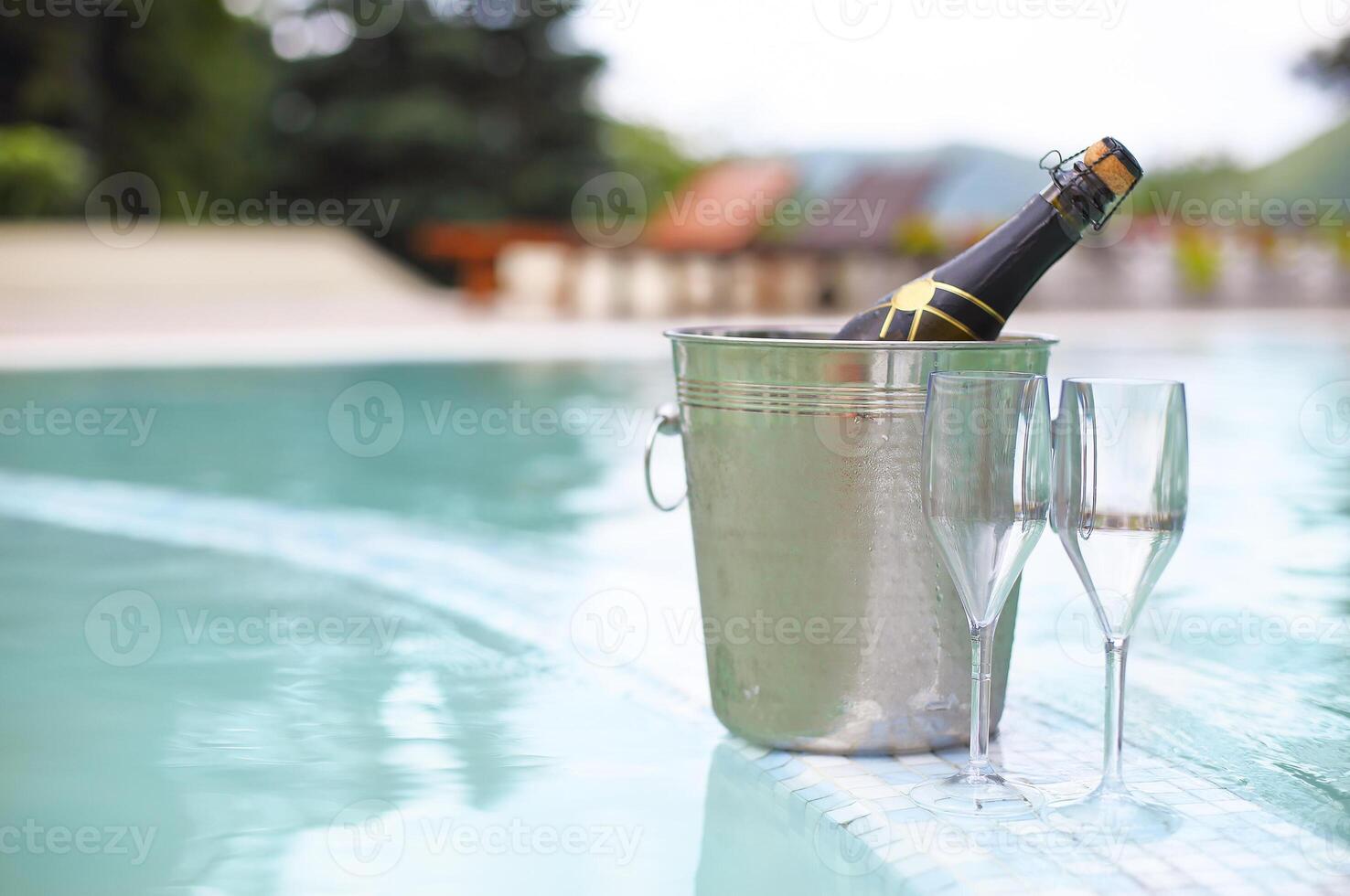 Ice bucket champagne bottle and two glasses near pool photo