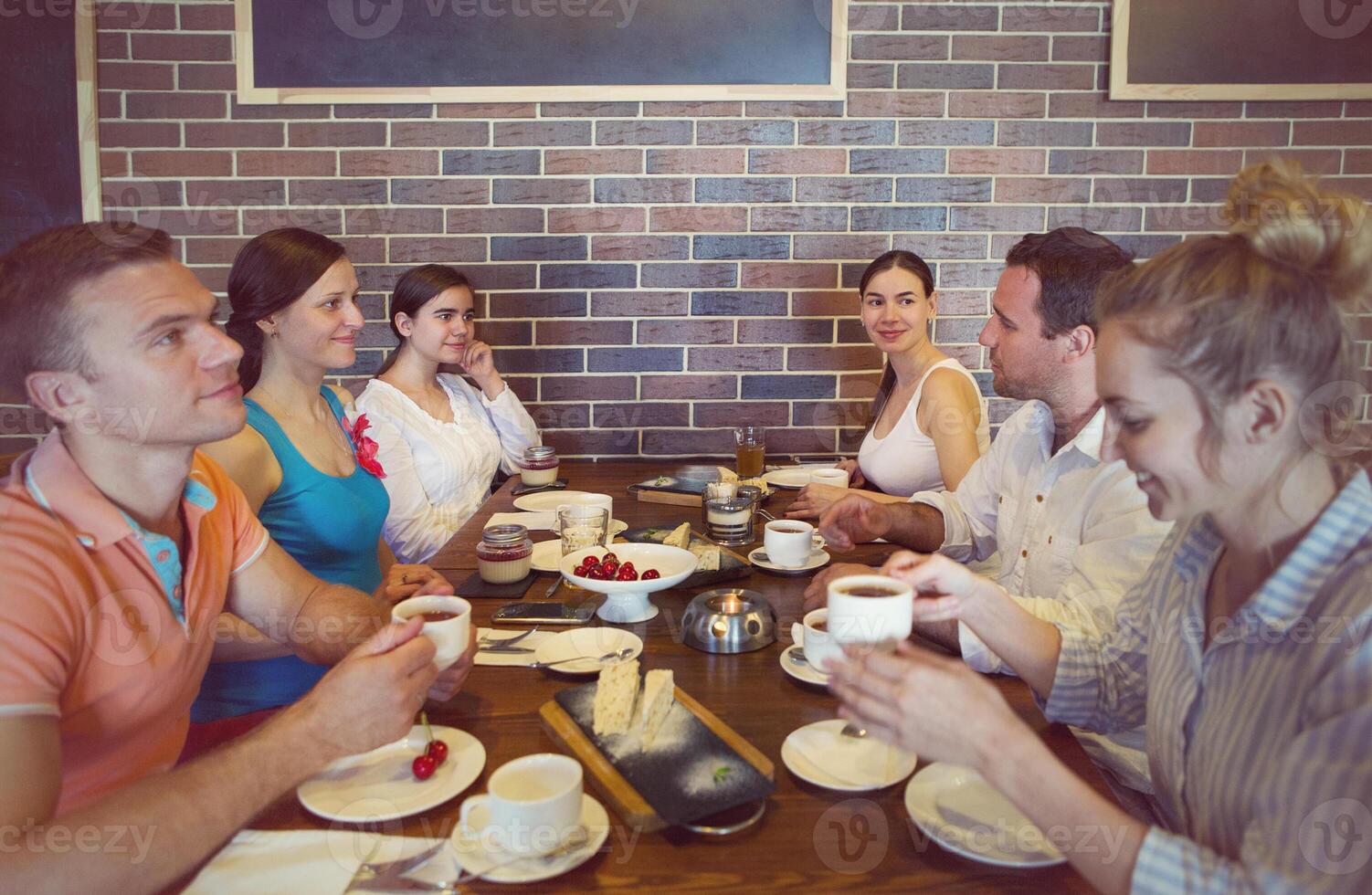 Six cheerful friends chatting while lunch in restaurant photo