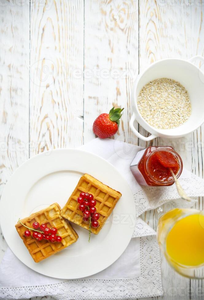 Waffles with red currant jam and berries, orange juice and oat flakes oatmeal photo