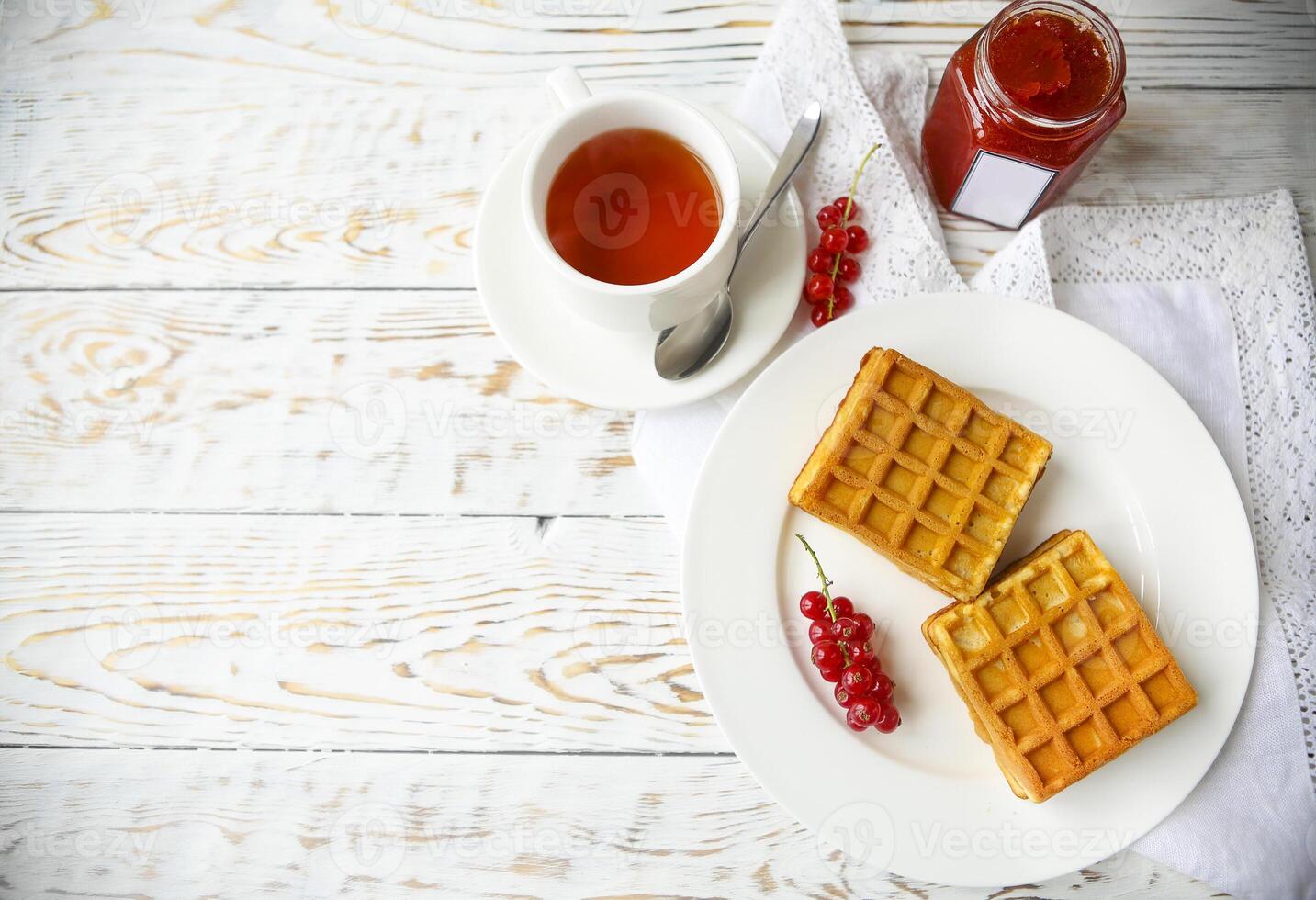 Waffles with red currant jam and berries on a white plate on the wooden background photo