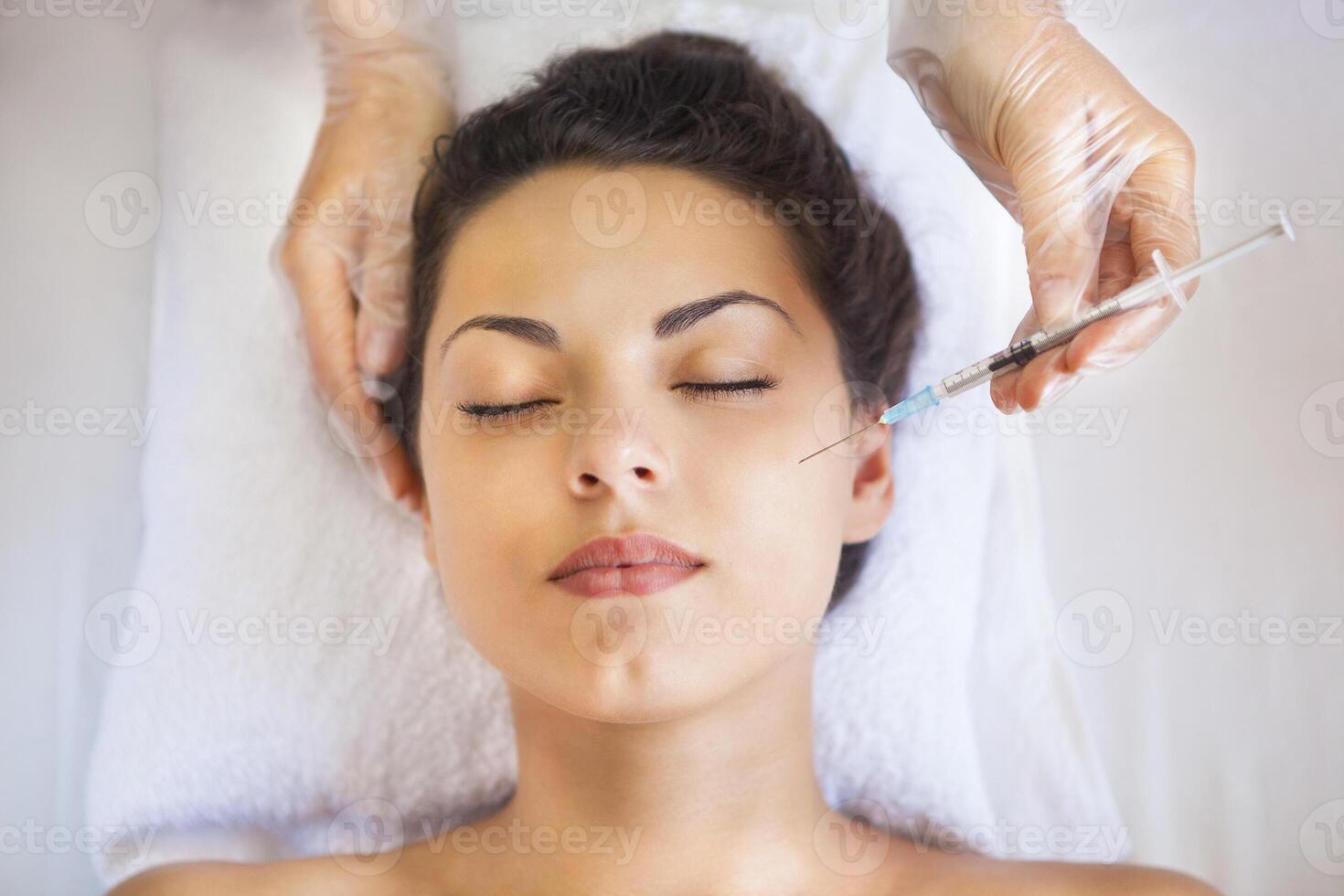 Young pretty woman getting cosmetic injection in the face like a part of the clinic treatment photo