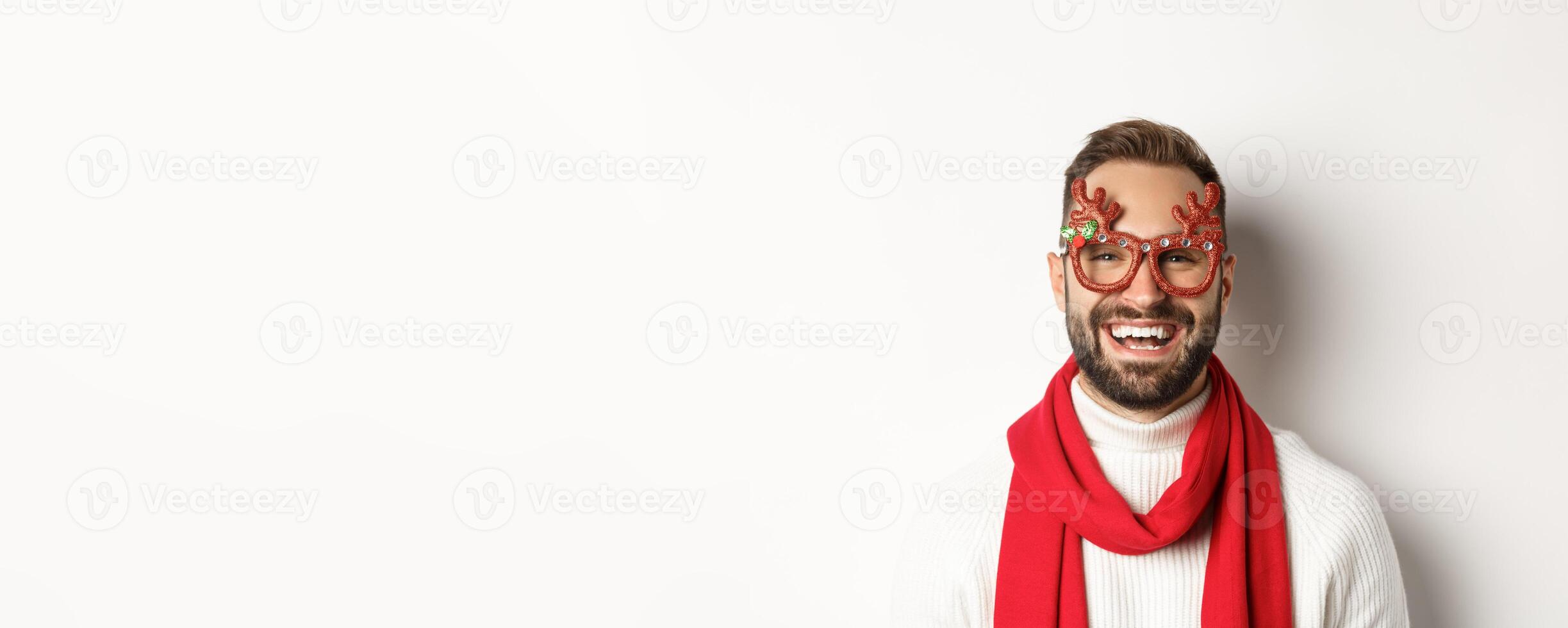 Christmas, New Year and celebration concept. Close-up of happy bearded man smiling, wearing party glasses and red scarf, white background photo
