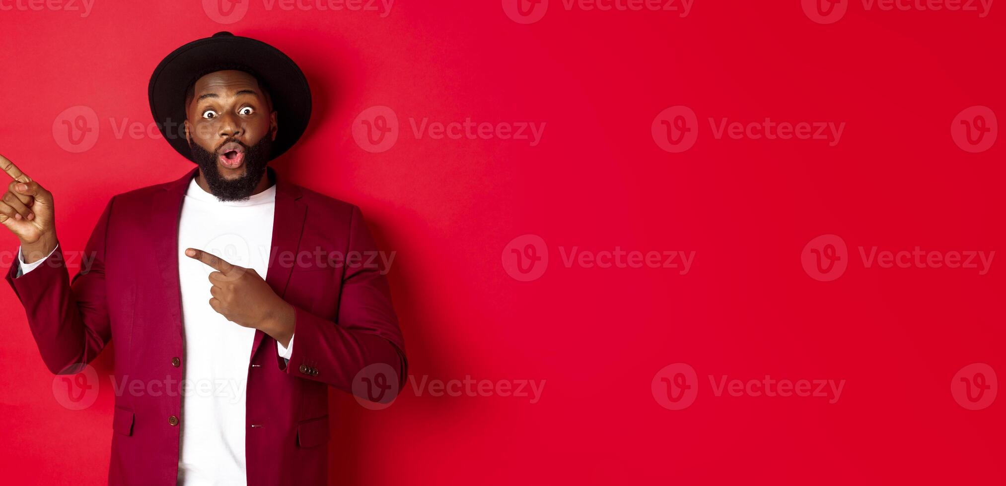 Winter holidays and shopping concept. Happy Black man pointing left and smiling, showing new year promo offer on red background photo