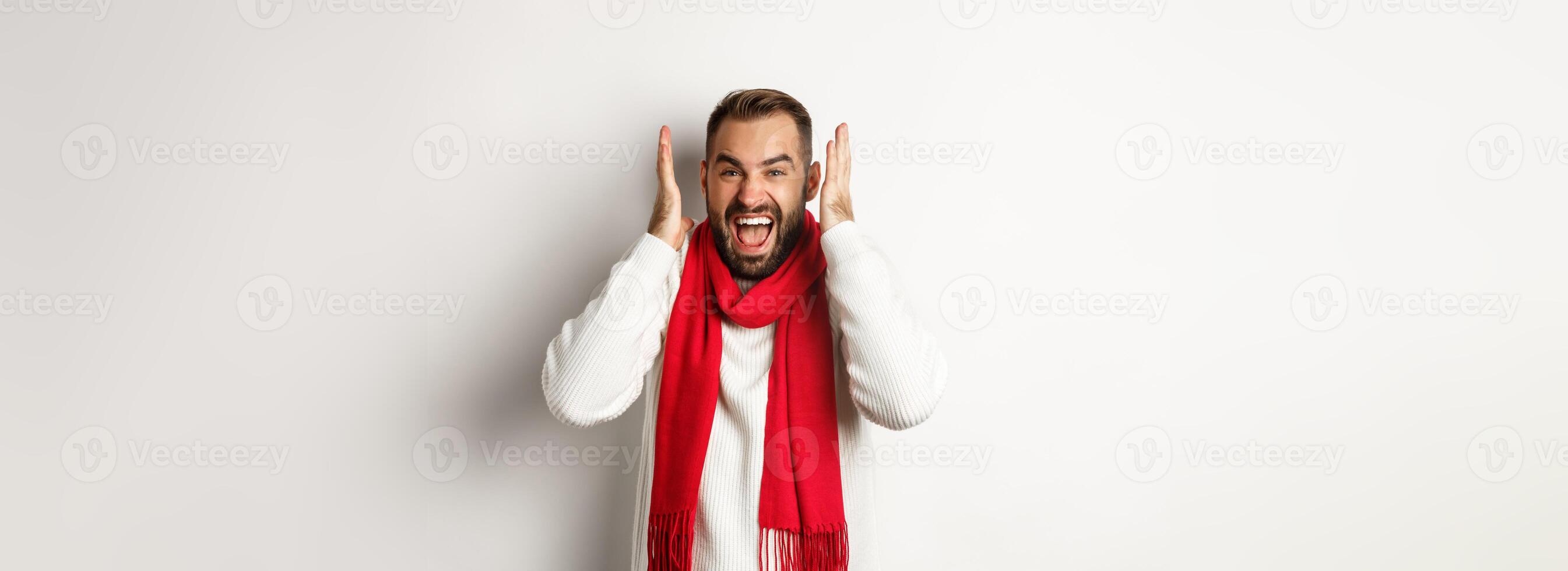 Christmas holidays and New Year concept. Angry man in scream and shout, shaking hands near head with frustrated expression, standing over white background photo
