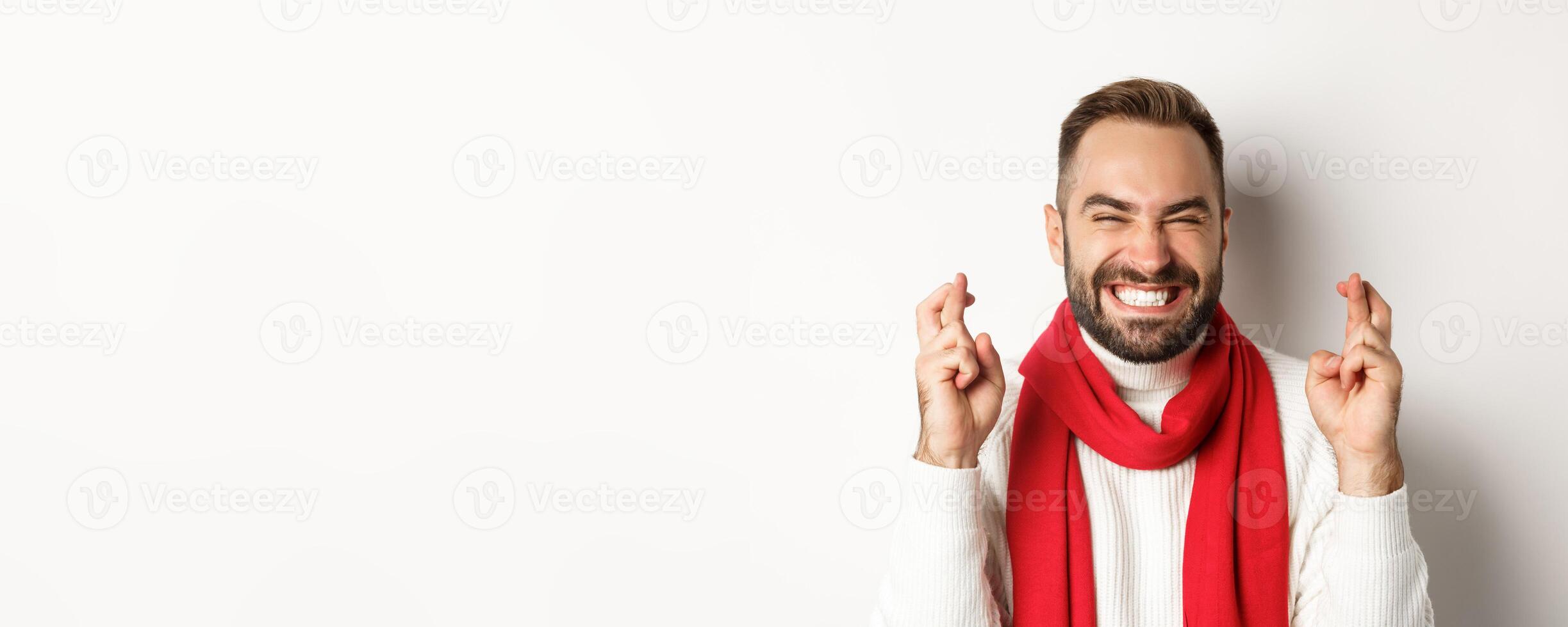 Christmas holidays. Happy attractive man making wish on winter holidays, cross fingers for good luck, standing over white background photo