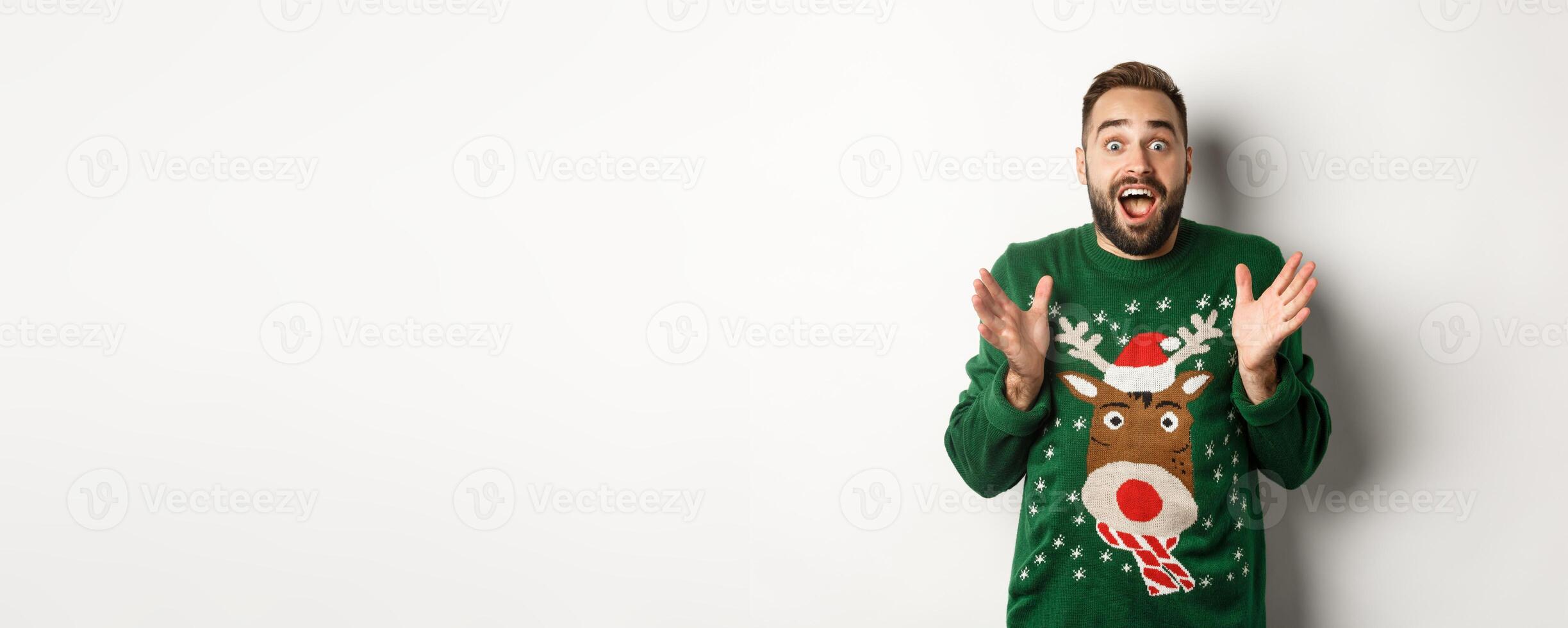 New year celebration and winter holidays concept. Happy and surprised bearded guy looking amazed, catching something, standing in funny Christmas sweater, white background photo