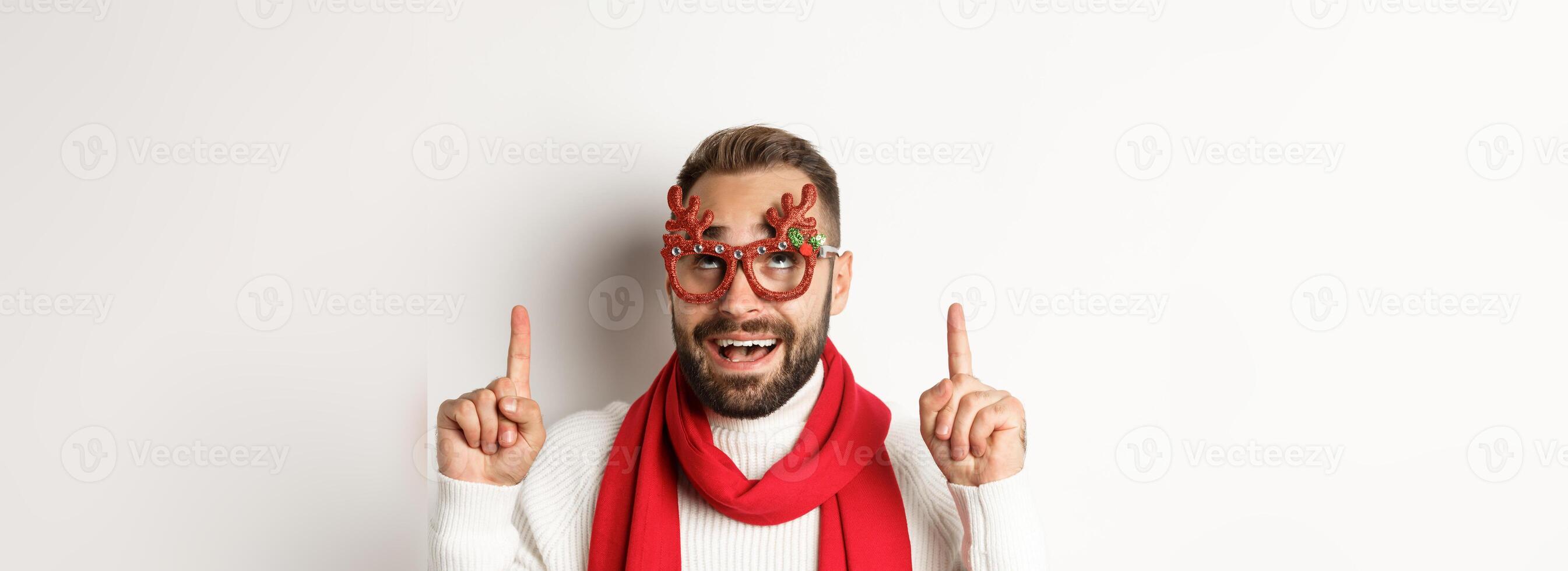 Christmas, New Year and celebration concept. Close-up of excited bearded guy in party glasses, pointing and looking up at store promo, white background photo