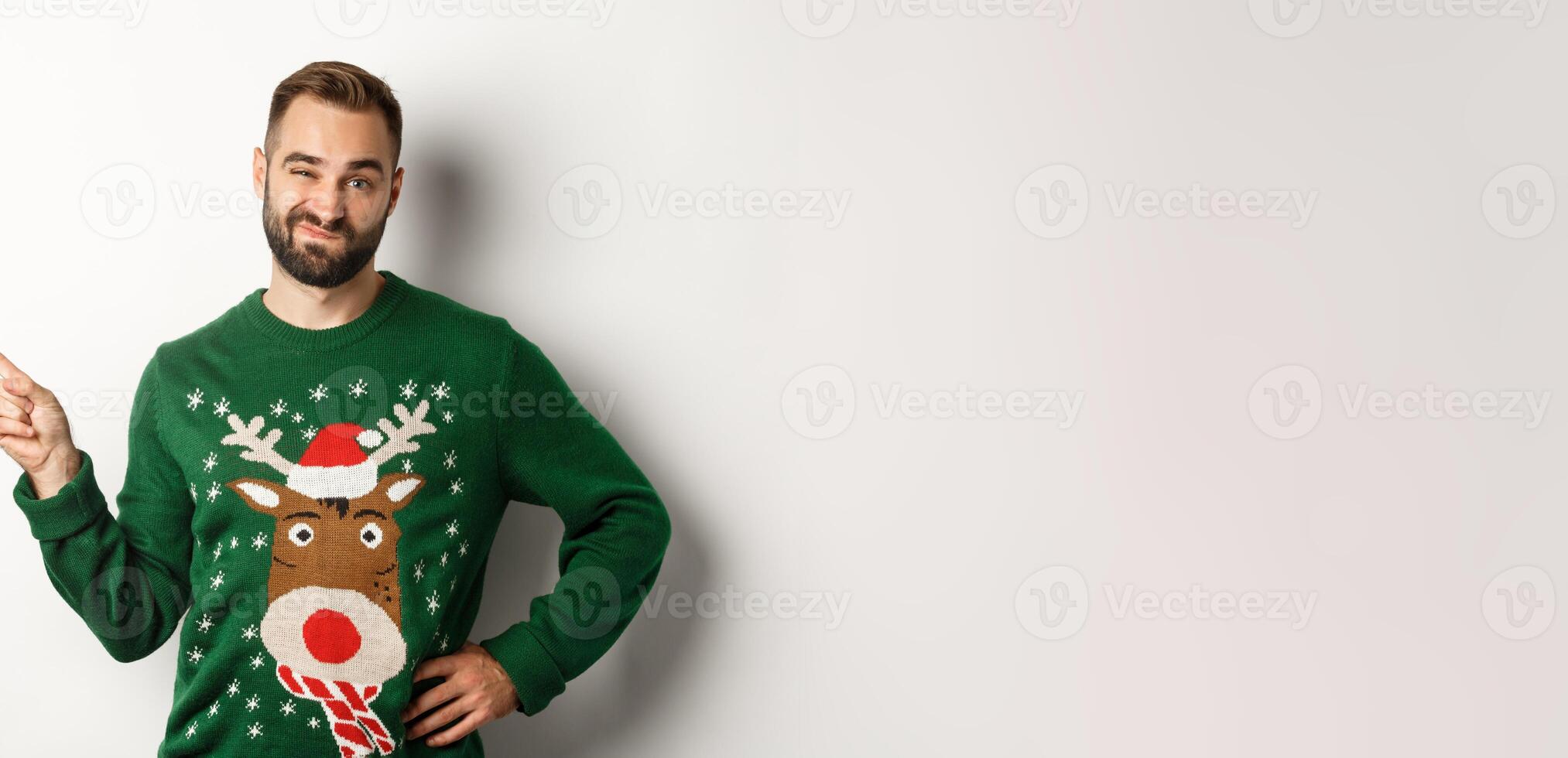 New year celebration and winter holidays concept. Skeptical guy in christmas sweater looking displeased, pointing finger at upper left corner product, dislike it, white background photo