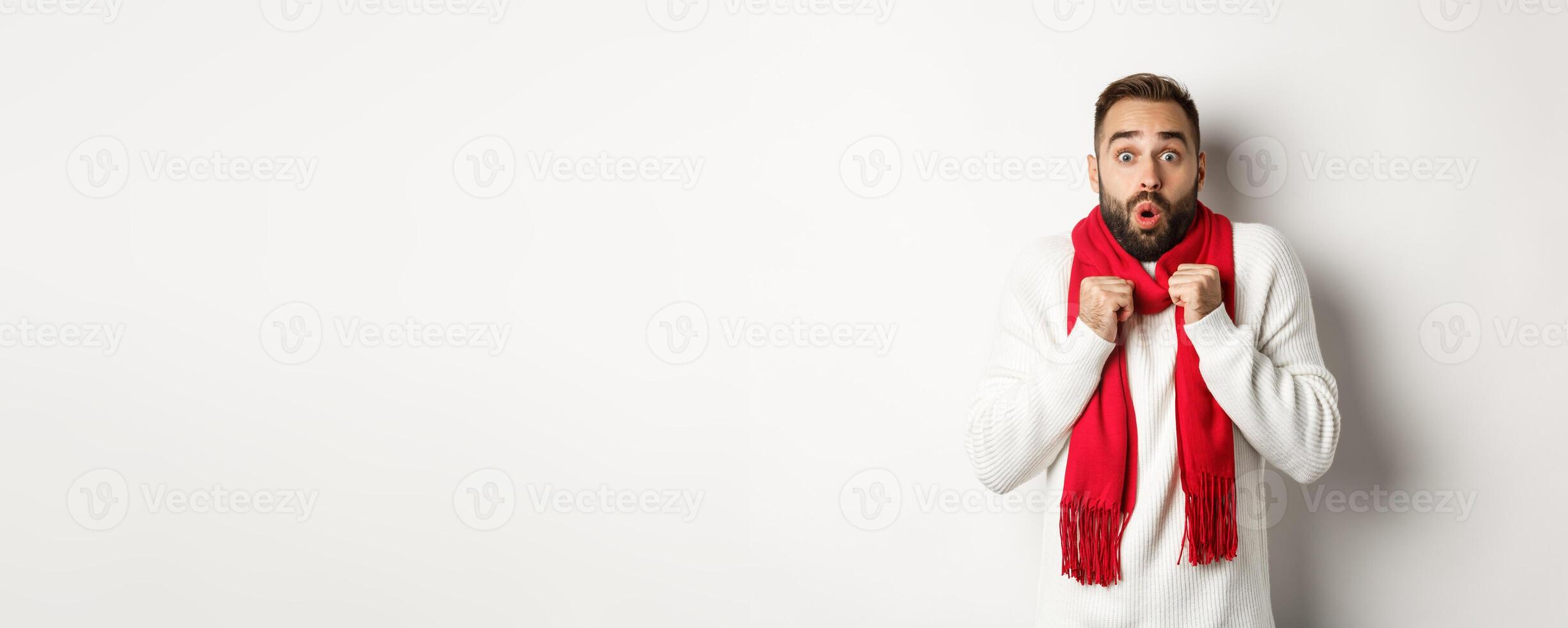 Christmas holidays and celebration concept. Man looking in awe at camera, standing surprised, feeling cold on new year, wearing red scarf and sweater, white background photo