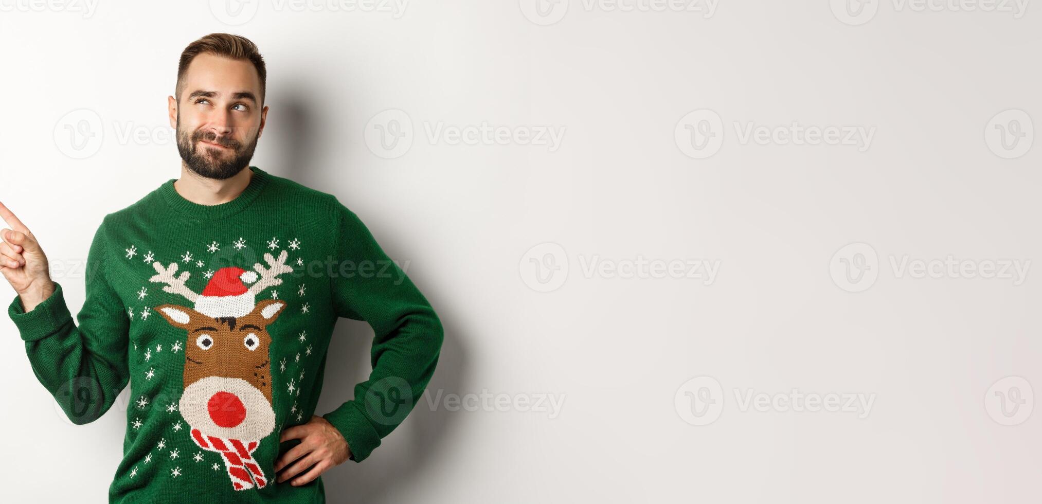 Winter holidays and christmas. Thoughtful bearded man thinking, having an idea and pointing finger at upper left corner, white background photo