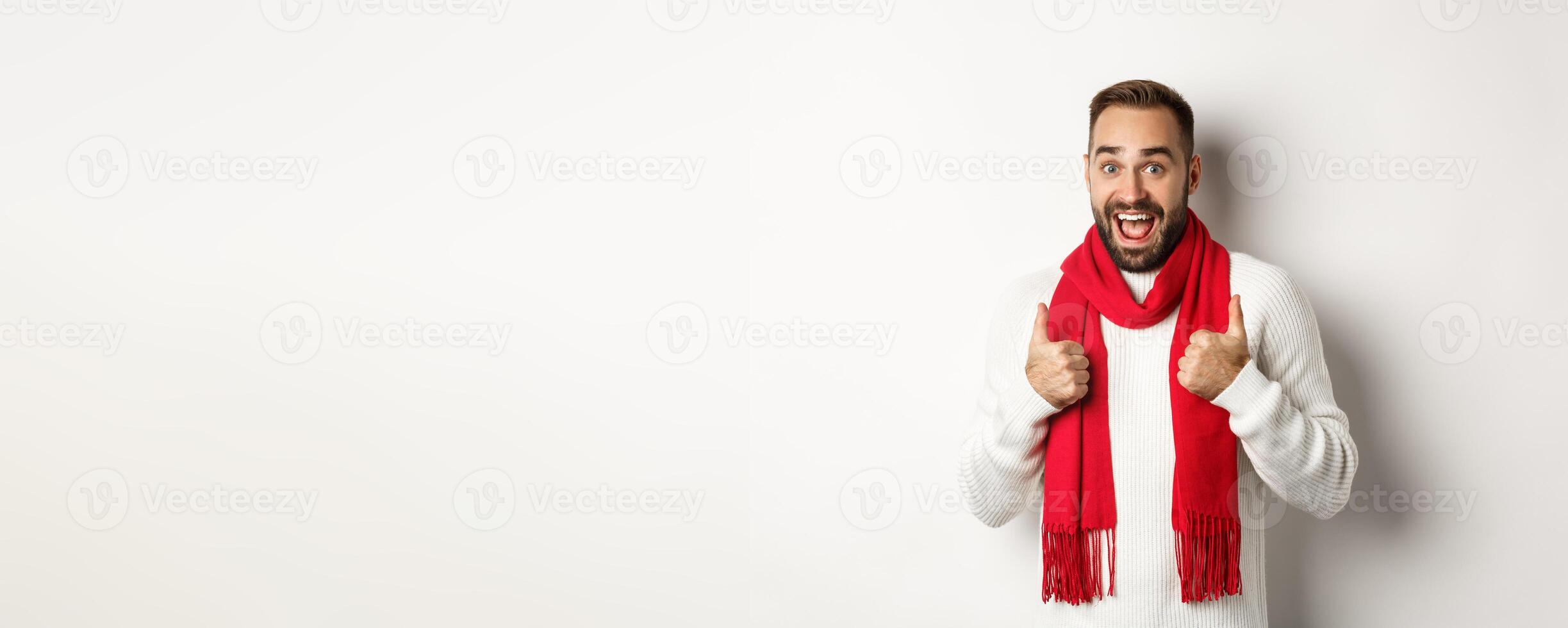 Winter holidays and shopping concept. Cheerful bearded man like everything, showing thumbs up in approval, standing amazed against white background photo