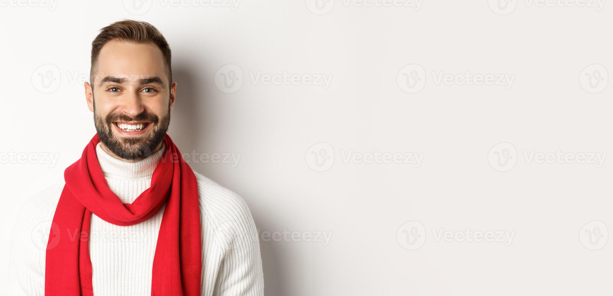 Christmas holidays. Handsome bearded man in red scarf and sweater smiling, white background photo