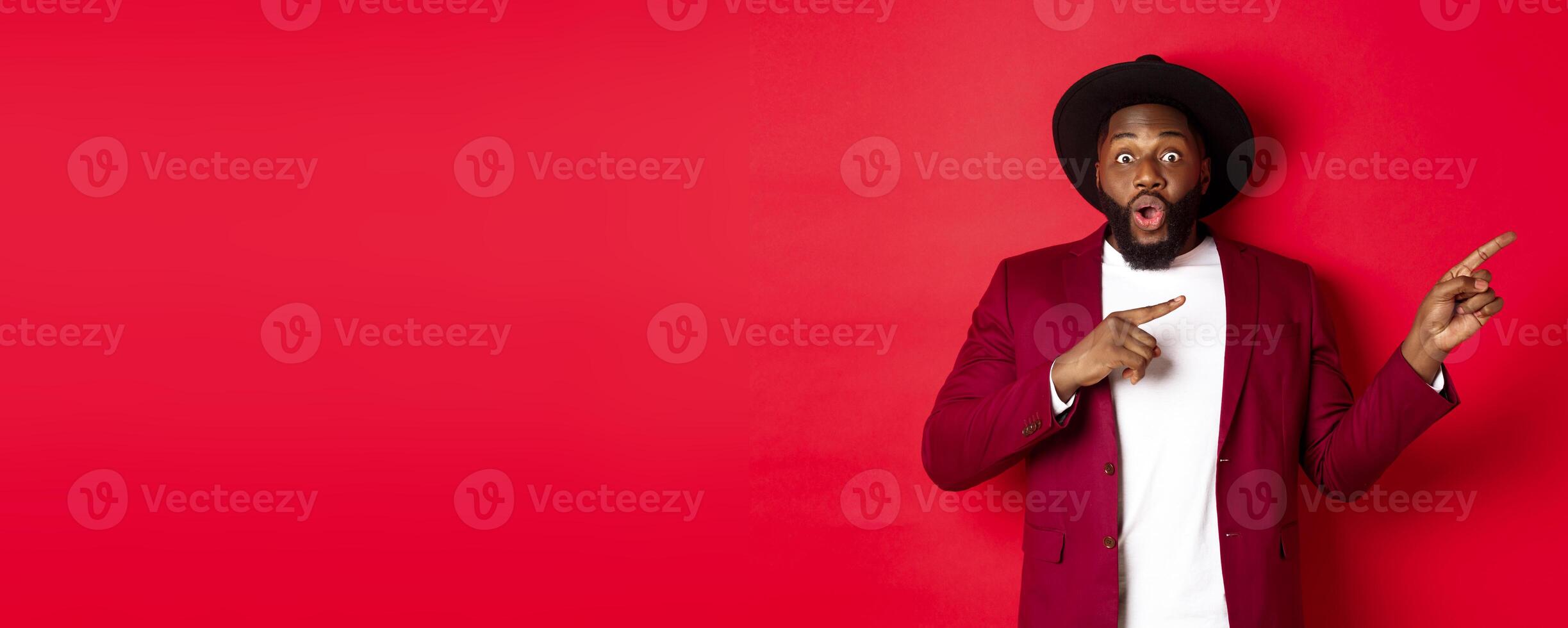 Winter holidays and shopping concept. Stylish african american man pointing fingers right at copy space for logo, standing over red background photo