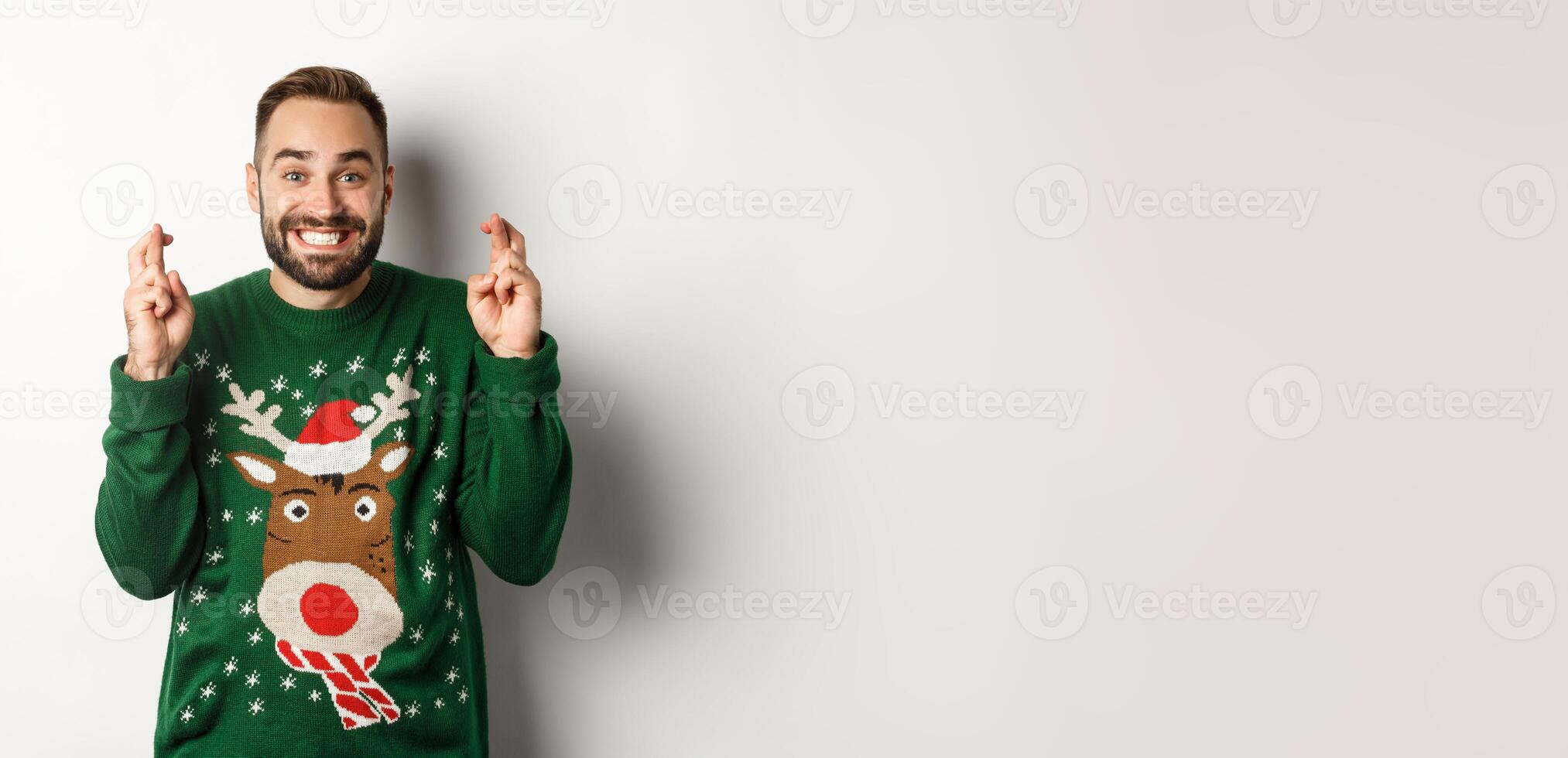 Christmas, holidays and celebration. Hopeful happy guy making wish, keep fingers crossed for good luck and smiling, standing over white background photo