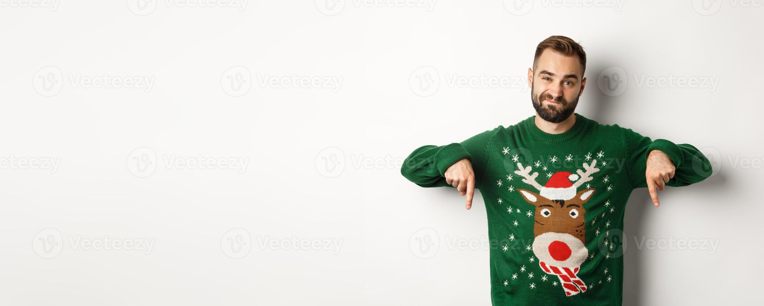 Winter holidays and christmas. Skeptical bearded man looking disappointed, pointing fingers down in dislike of promo, standing over white background photo