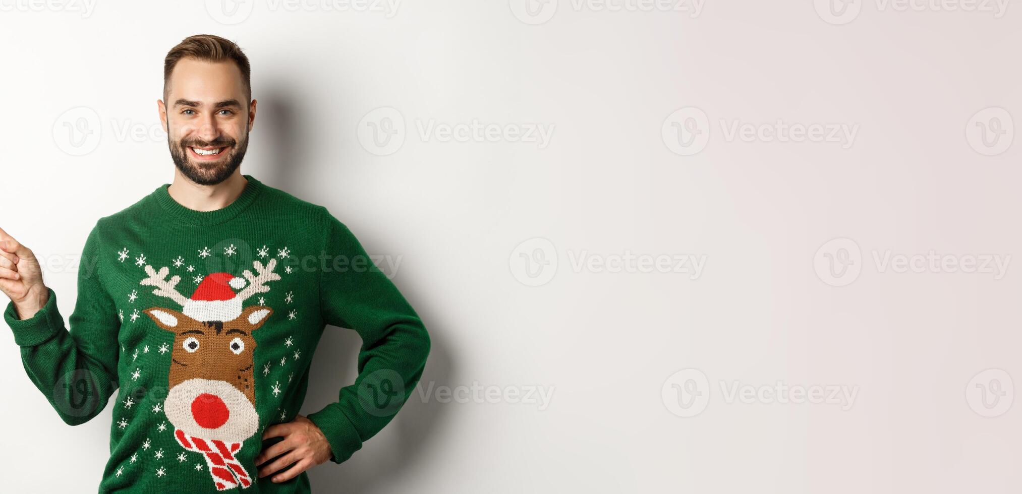 New year celebration and winter holidays concept. Confident and happy man with beard, wearing christmas sweater, pointing at upper left corner banner, white background photo