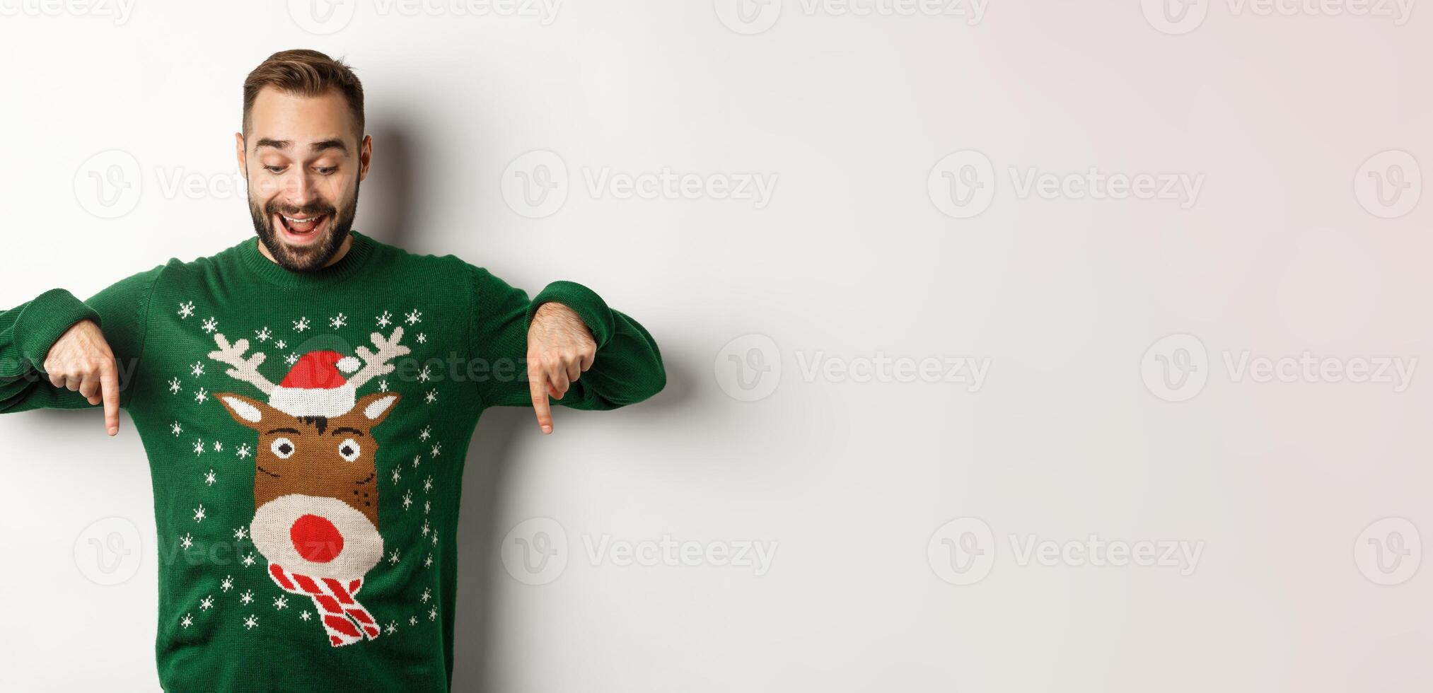Winter holidays and christmas. Happy bearded man in green sweater, looking and pointing fingers down at advertisement, showing copy space, white background photo