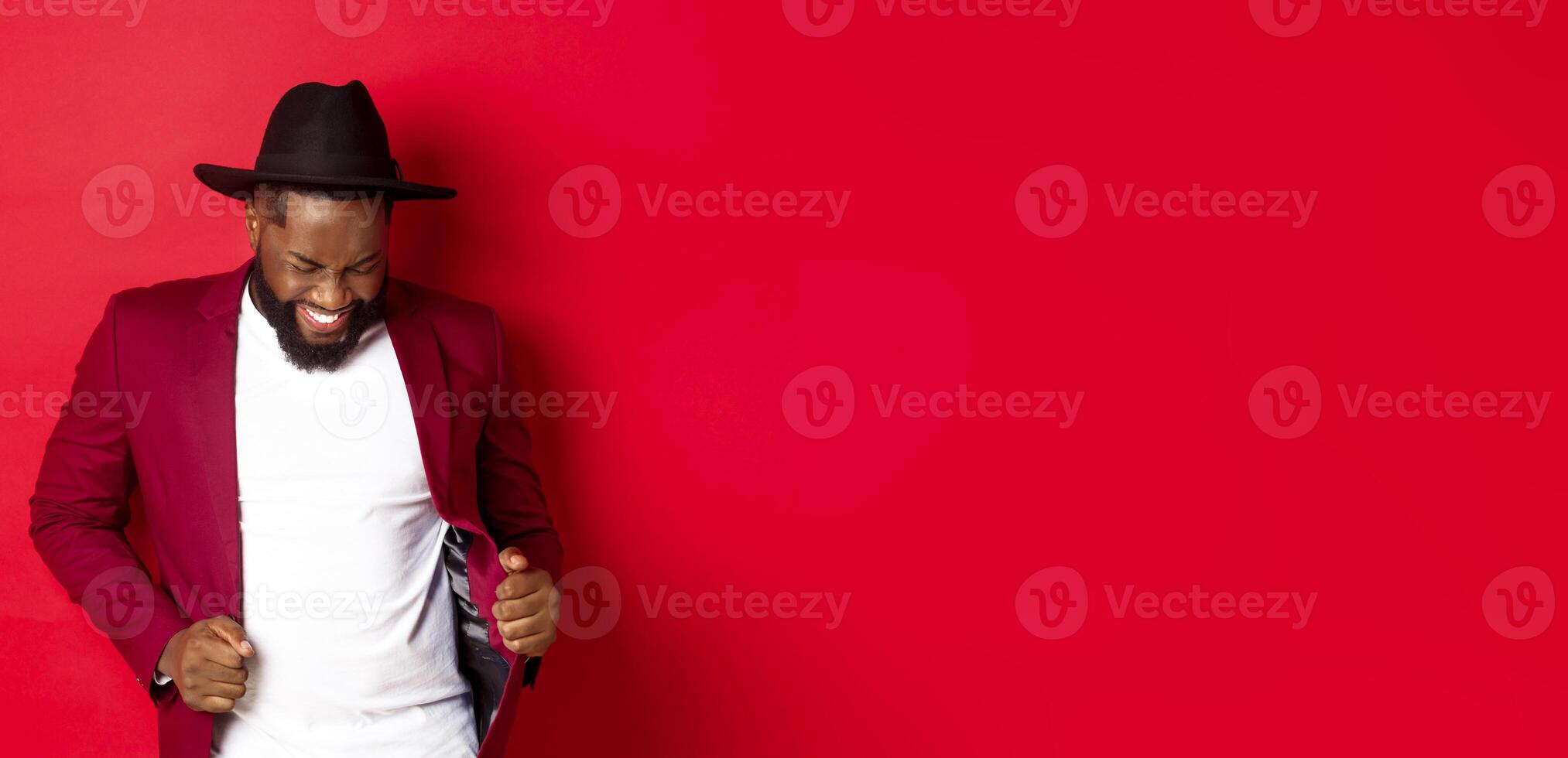 Christmas and people concept. Happy Black man celebrating New Year and dancing, wearing party outfit, red background photo
