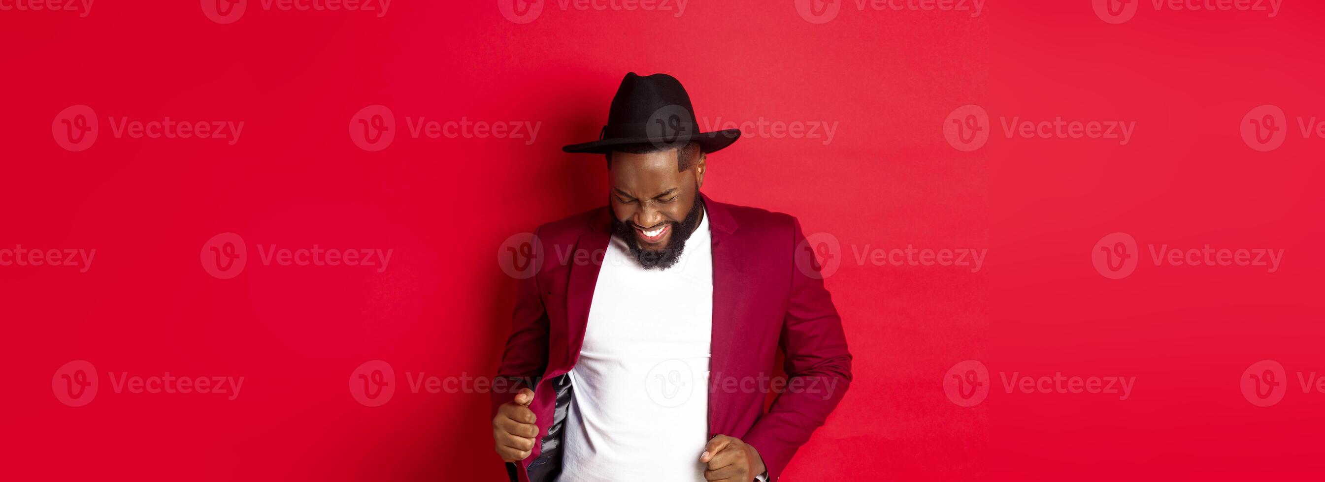 Christmas and people concept. Happy Black man celebrating New Year and dancing, wearing party outfit, red background photo