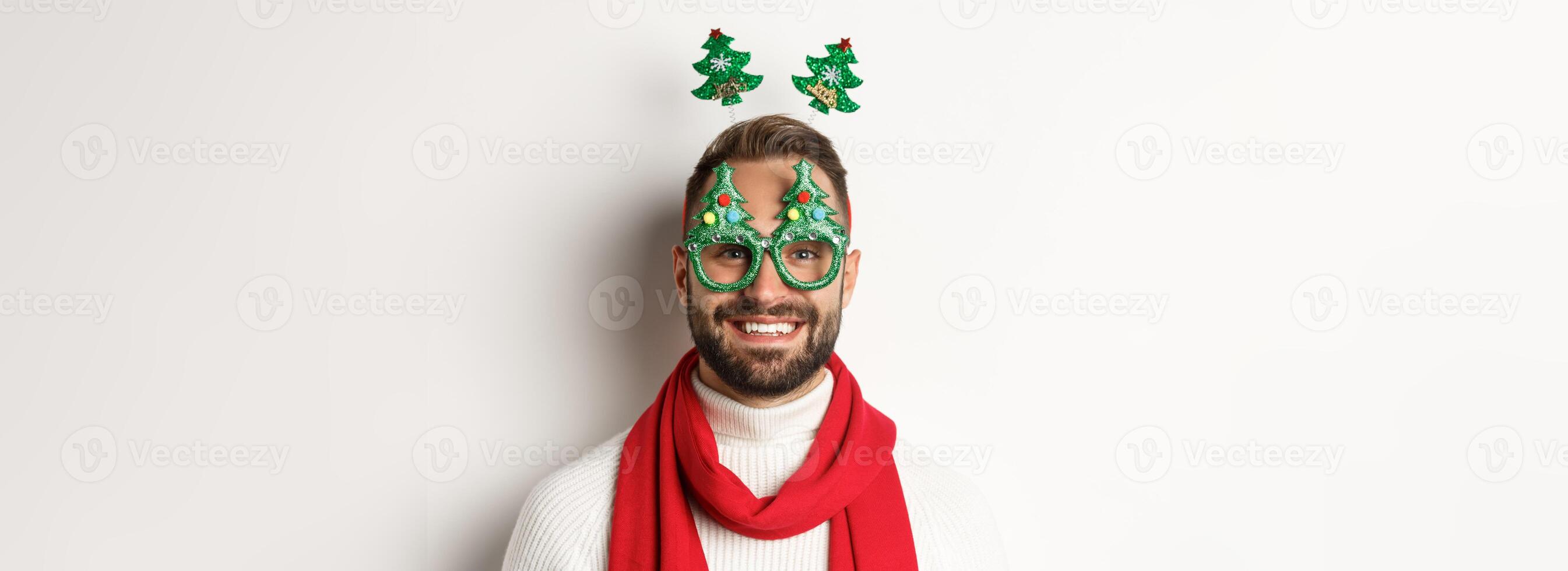 Christmas, New Year and celebration concept. Close-up of handsome bearded man in funny party glasses looking happy, standing against white background photo