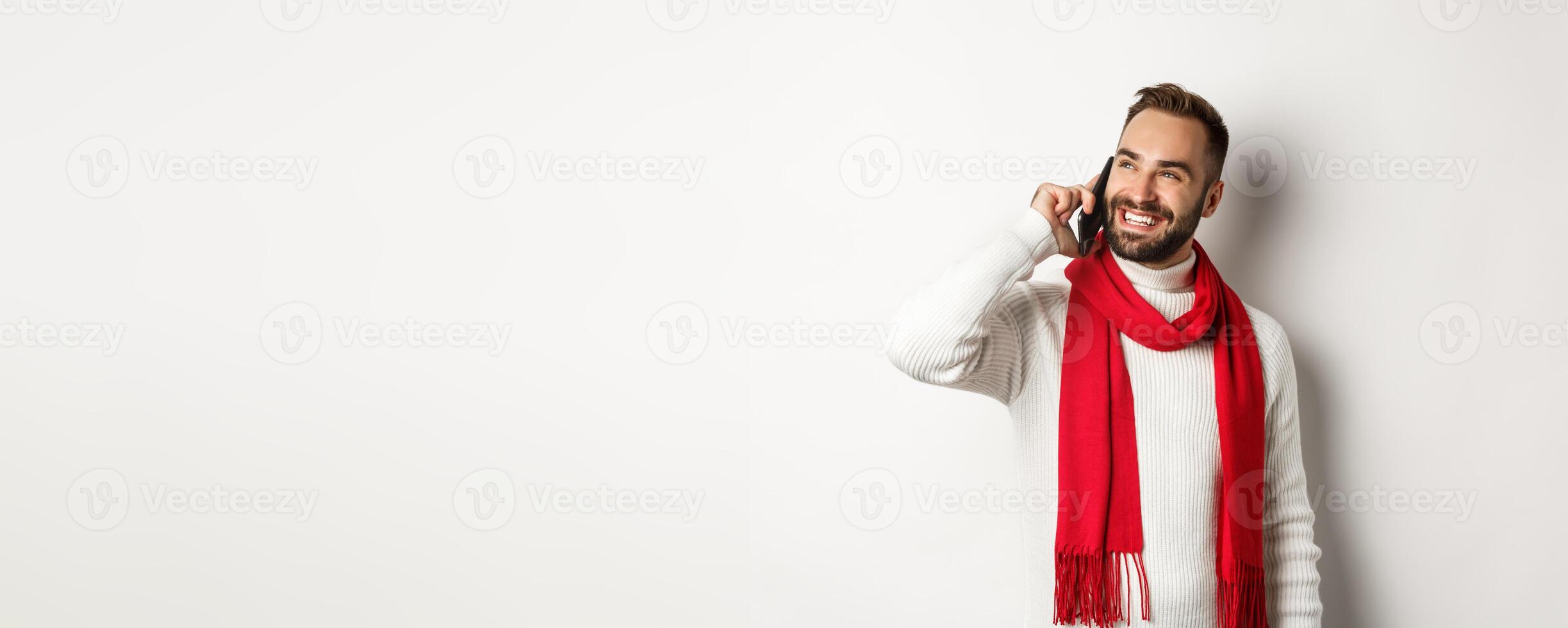 Handsome smiling man talking on phone, looking satisfied, standing in winter scarf and sweater, white background photo
