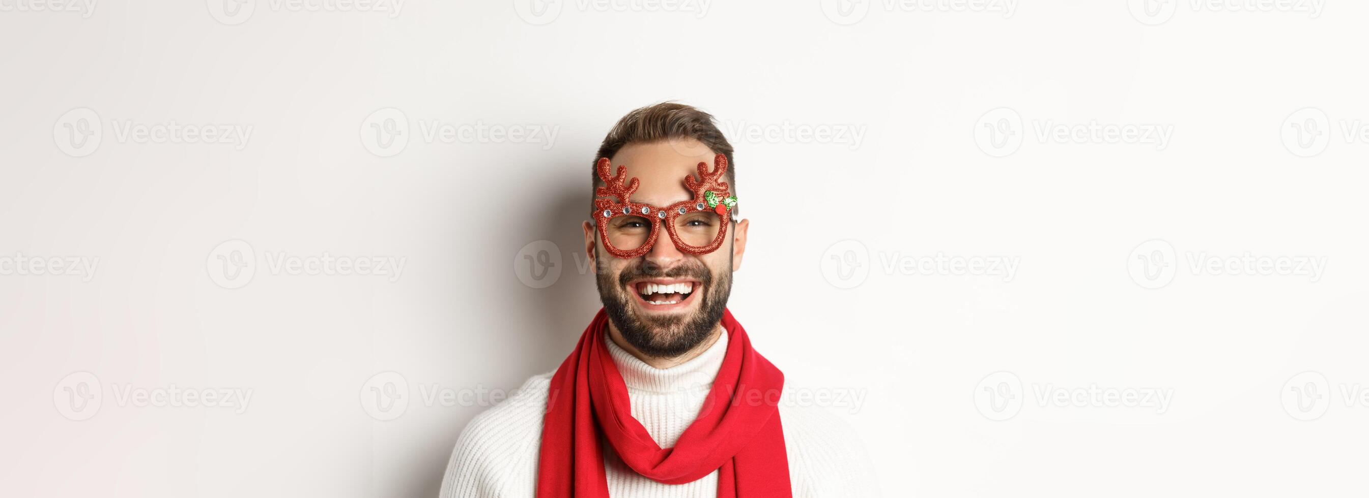 Christmas, New Year and celebration concept. Close-up of happy bearded man smiling, wearing party glasses and red scarf, white background photo