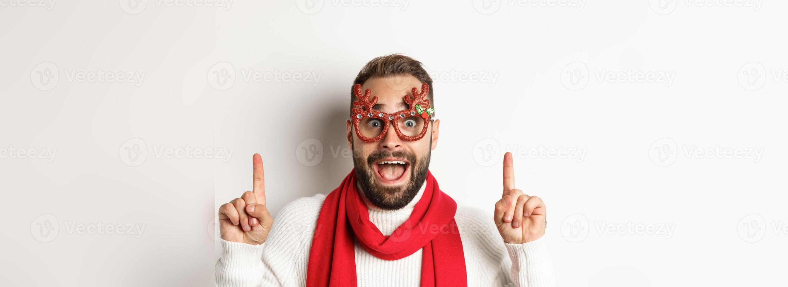 Christmas, New Year and celebration concept. Close-up of handsome bearded man in party glasses and red scarf, celebrate winter holidays and pointing fingers up at copy space photo