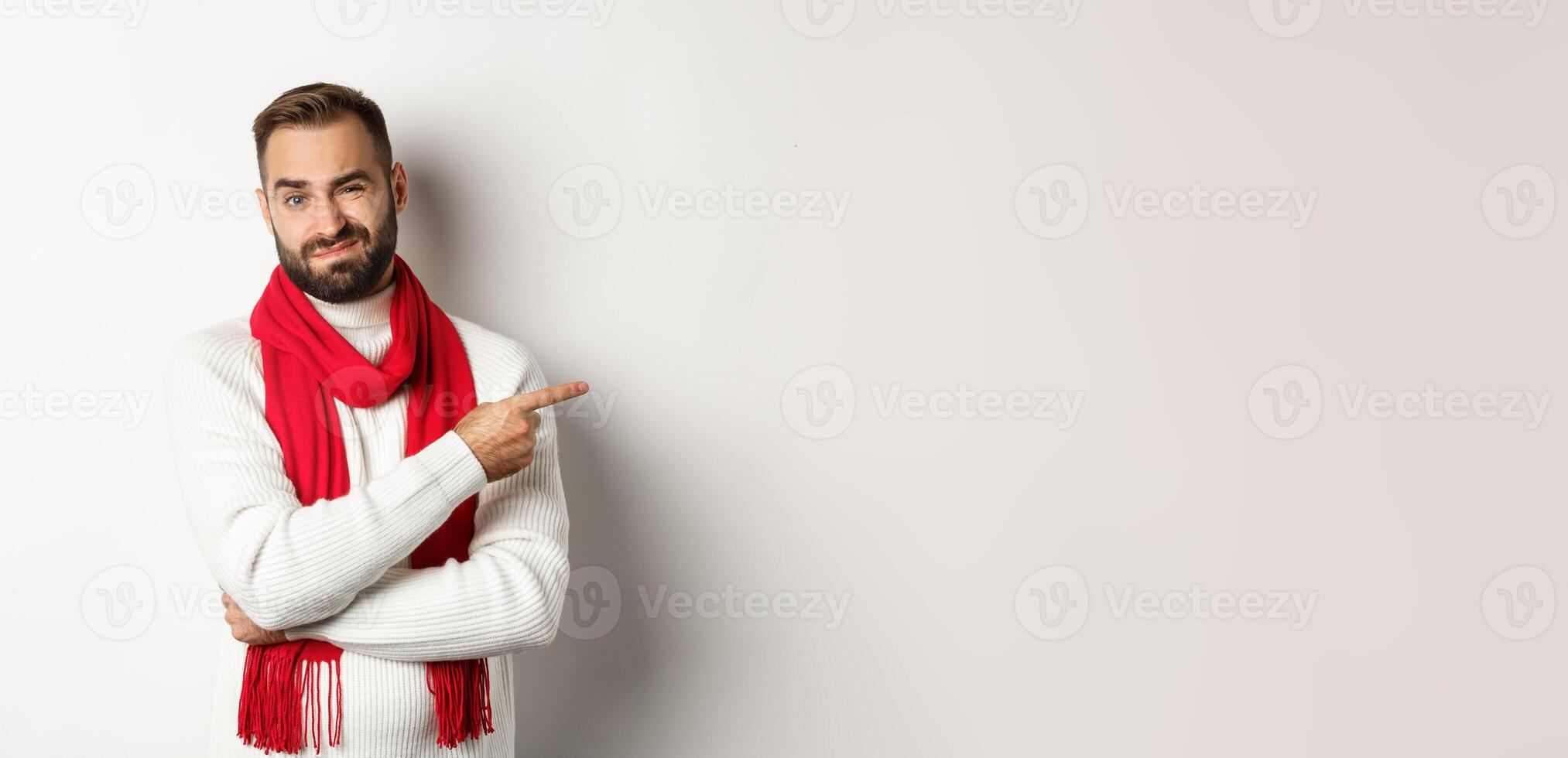 Christmas shopping and winter holidays concept. Displeased man pointing finger right and grimacing dissatisfied, standing skeptical against white background photo