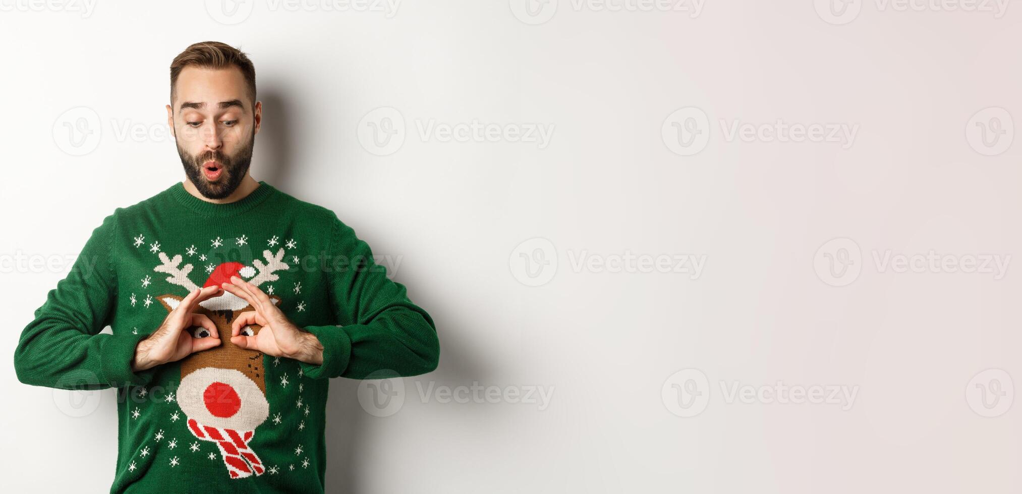 New Year, holidays and celebration. Happy young man making fun of his sweater and smiling, fool around on Christmas party, standing over white background photo