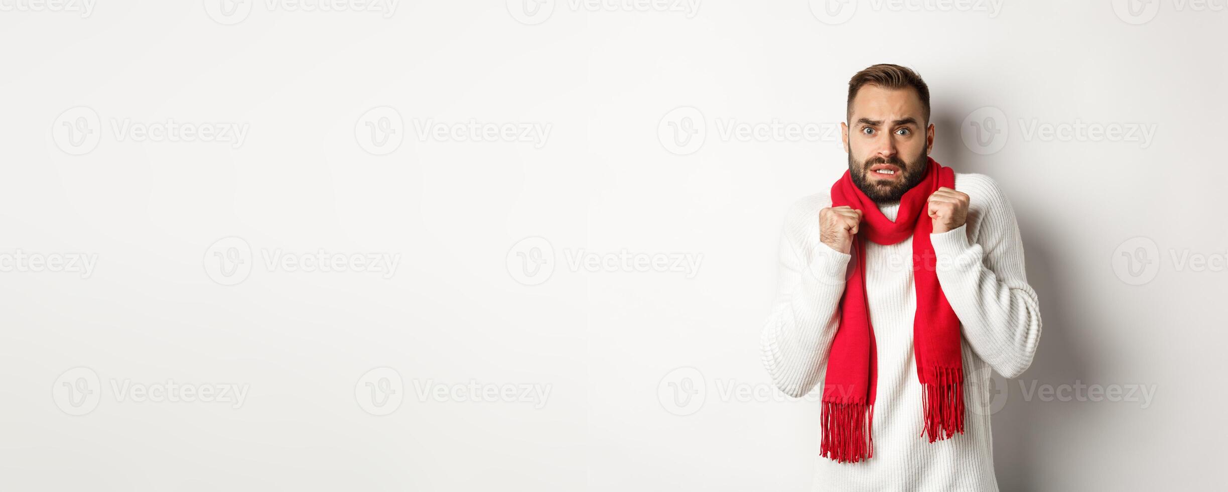 Christmas holidays and celebration concept. Scared man trembling from fear and looking startled, standing anxious in red scarf and white sweater photo