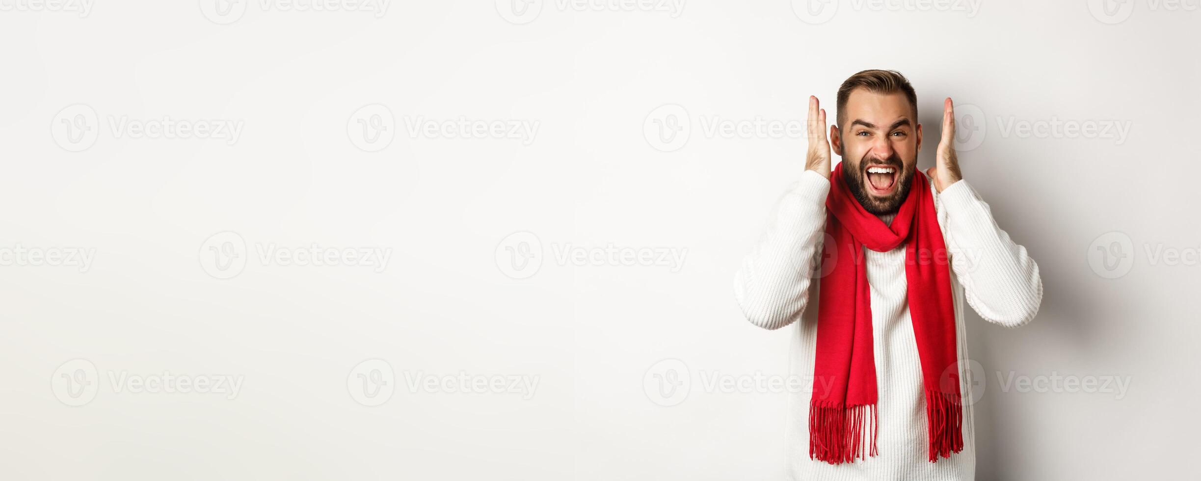 Christmas holidays and New Year concept. Angry man in scream and shout, shaking hands near head with frustrated expression, standing over white background photo