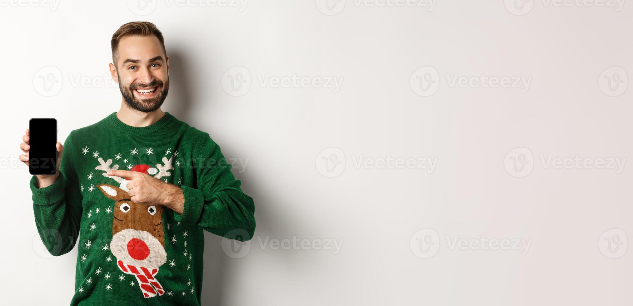 New Year, holidays and celebration. Handsome man smiling, pointing finger at mobile screen, showing app, standing over white background photo