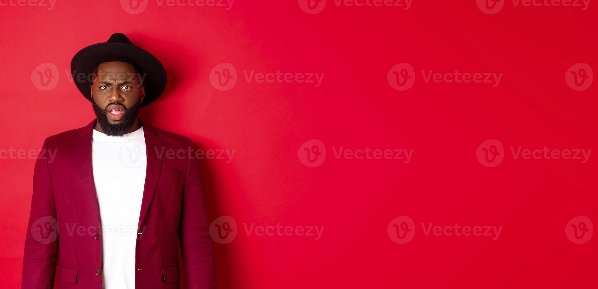 Fashion and party concept. Confused Black man in classy outfit frowning and staring at camera displeased, cant understand, standing over red background photo