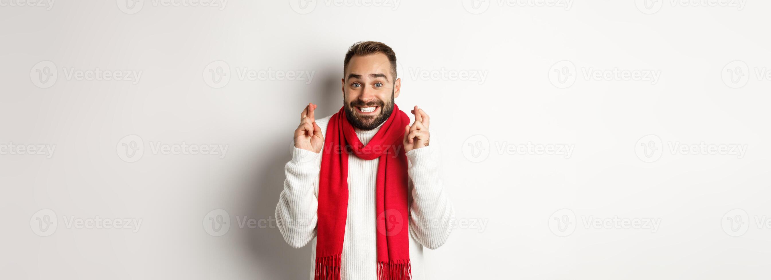 Christmas holidays and New Year concept. Hopeful man making wish with fingers crossed, waiting for gifts, standing over white background photo