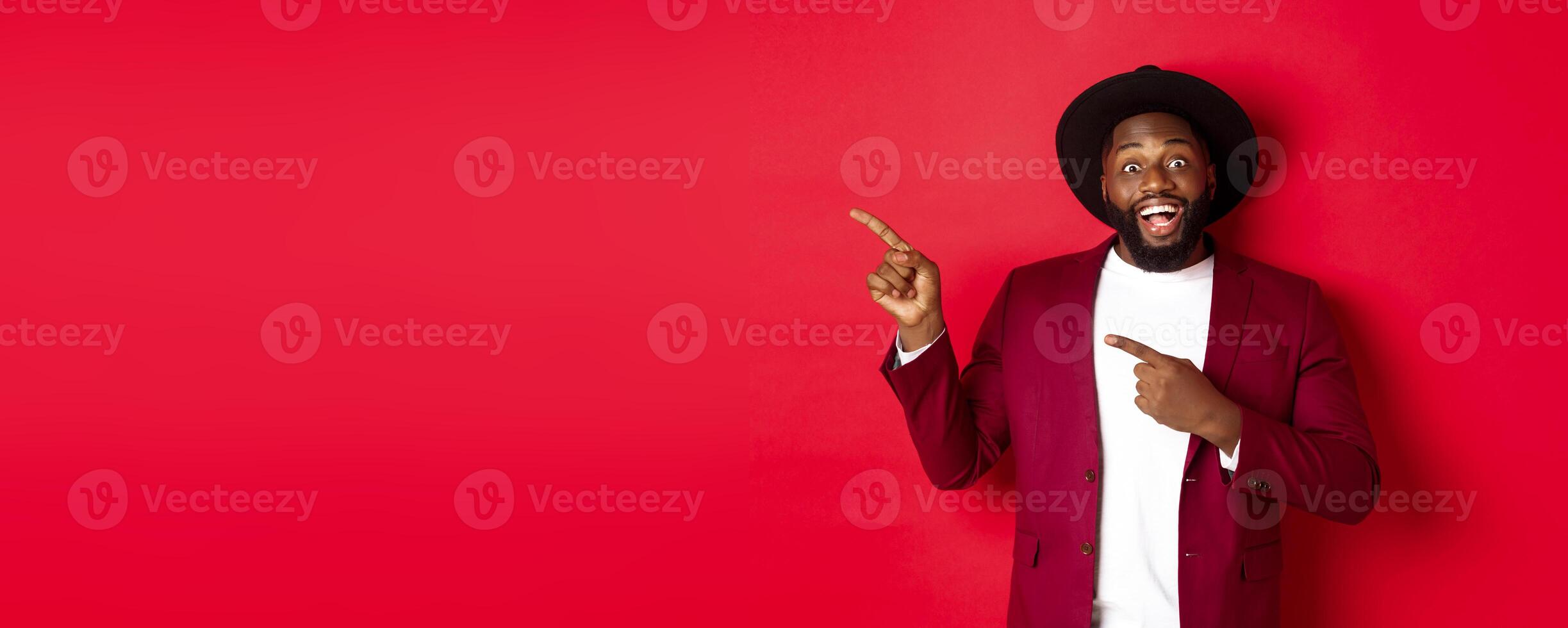 Winter holidays and shopping concept. Happy Black man pointing left and smiling, showing new year promo offer on red background photo