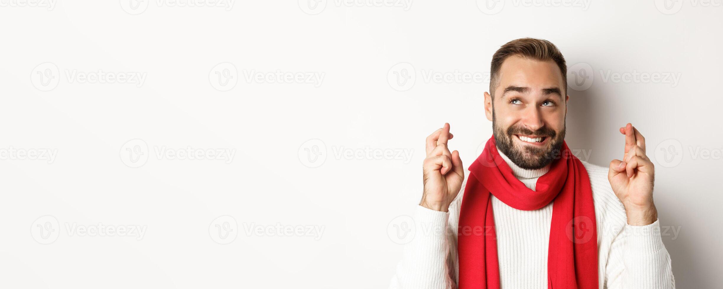 Christmas holidays. Happy attractive man making wish on winter holidays, cross fingers for good luck, looking up, standing over white background photo