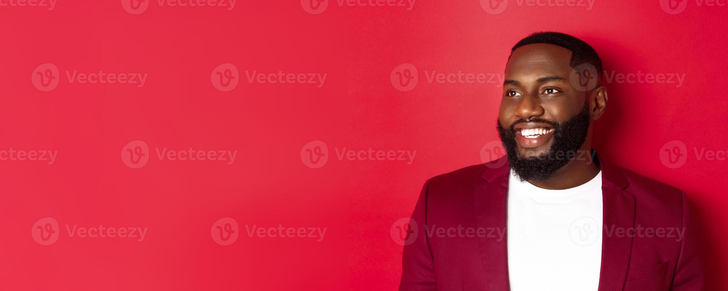 Close-up of handsome african american man with beard, looking left and smiling joyful, standing over red background photo