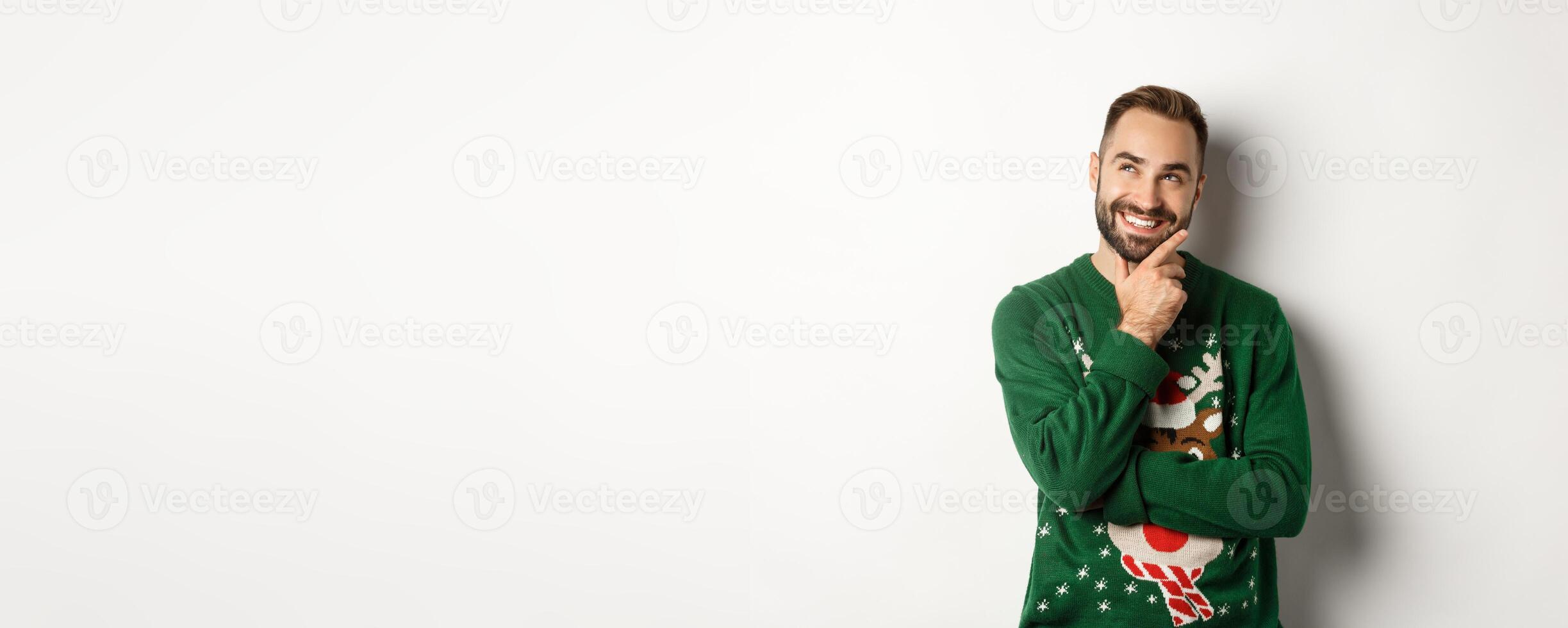 New year celebration and winter holidays concept. Thoughtful nice guy thinking about Christmas gifts, looking at upper left corner and smiling, white background photo