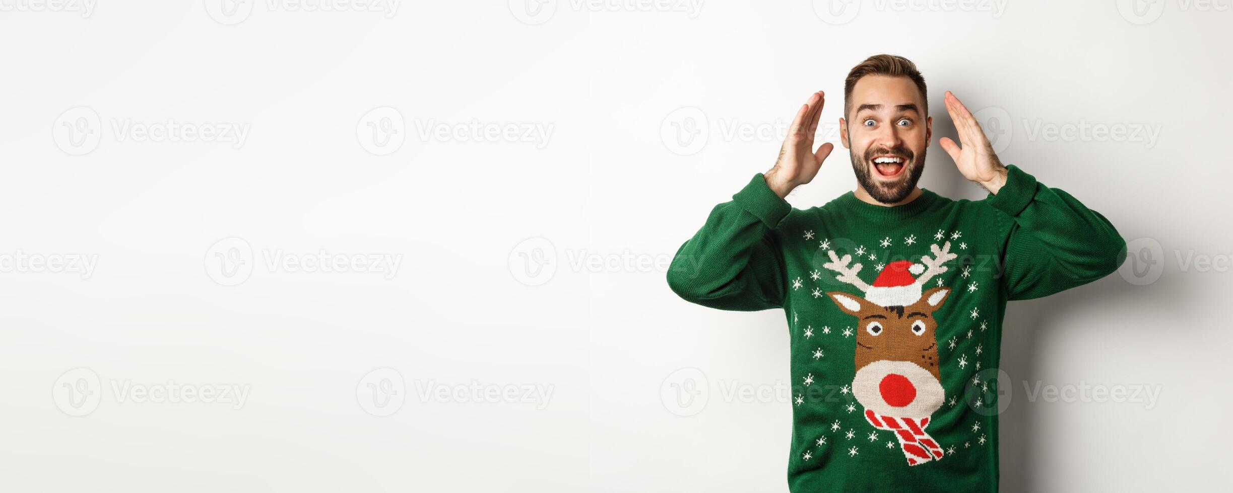 Christmas, holidays and celebration. Surprised man open eyes and see a gift, standing happy against white background photo