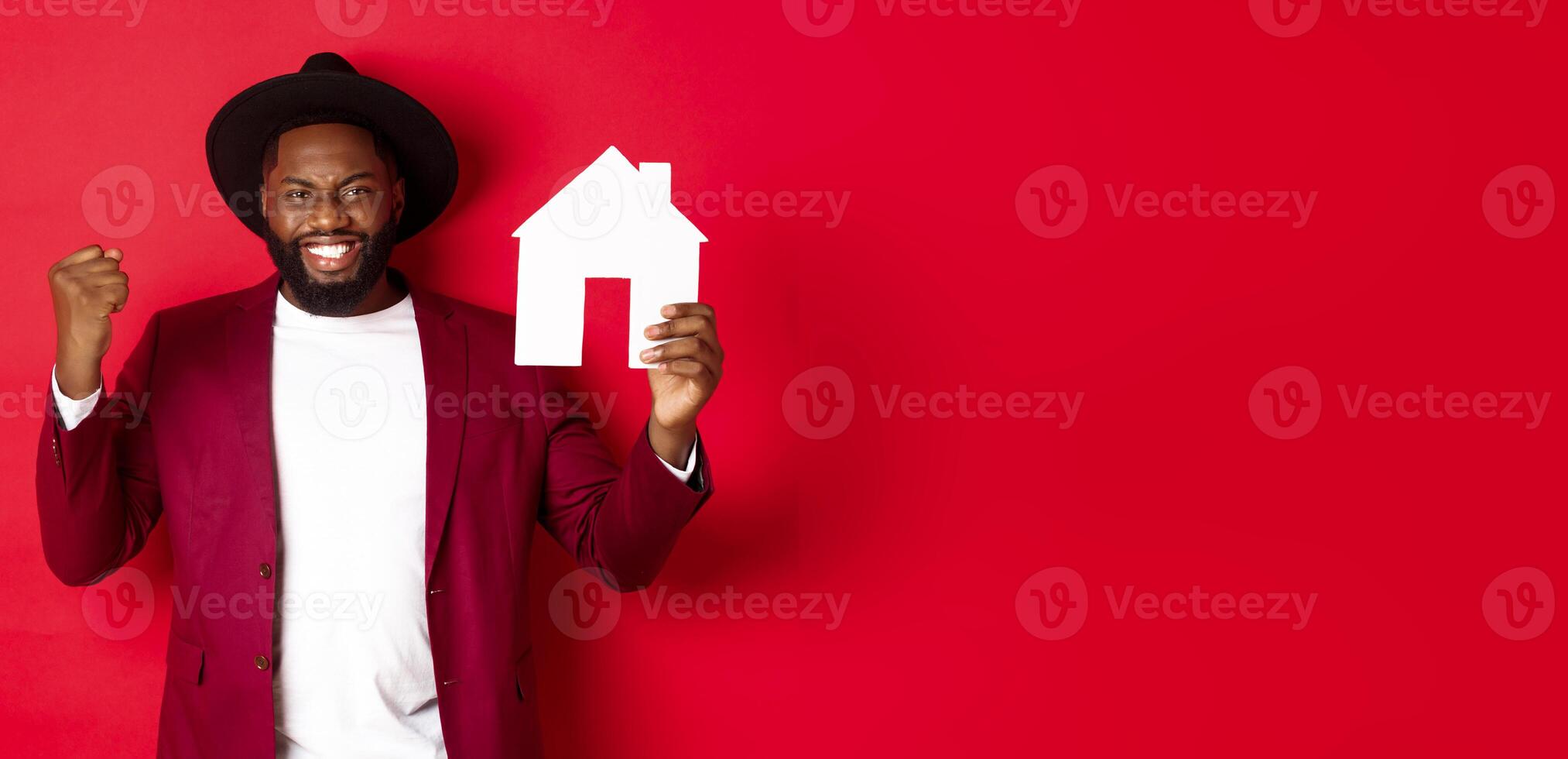 Real estate. Cheerful Black man rejoicing and showing paper home maket, standing over red background photo
