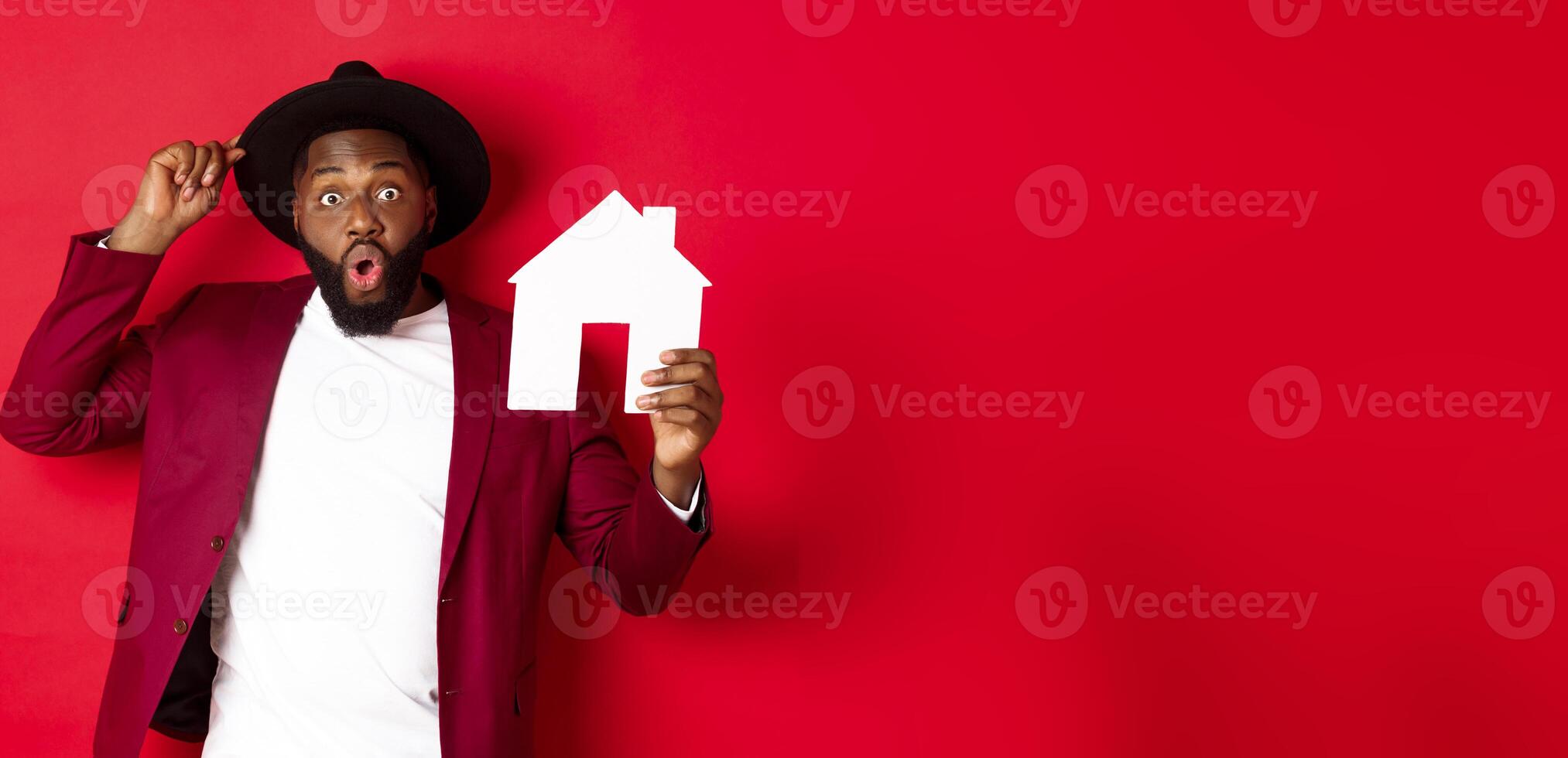 Real estate. Cheerful Black man showing paper house and smiling, recommending broker, standing over red background photo