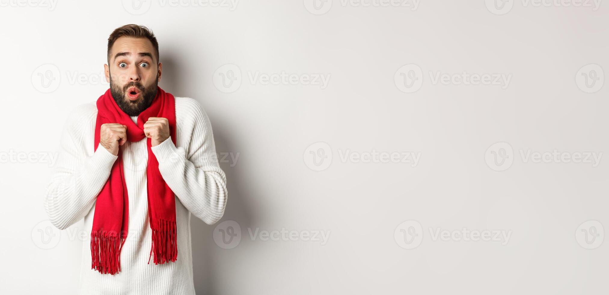 Christmas holidays and celebration concept. Man looking in awe at camera, standing surprised, feeling cold on new year, wearing red scarf and sweater, white background photo