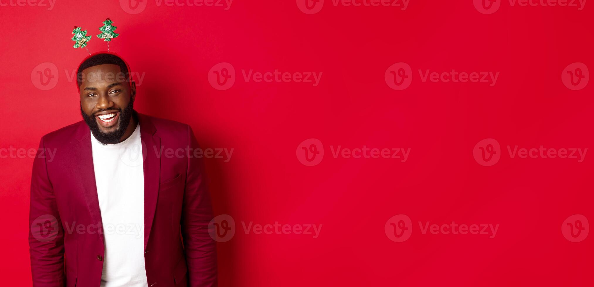 Merry Christmas. Handsome african american man in blazer and party headband, celebrating new year, smiling happy at camera, red background photo