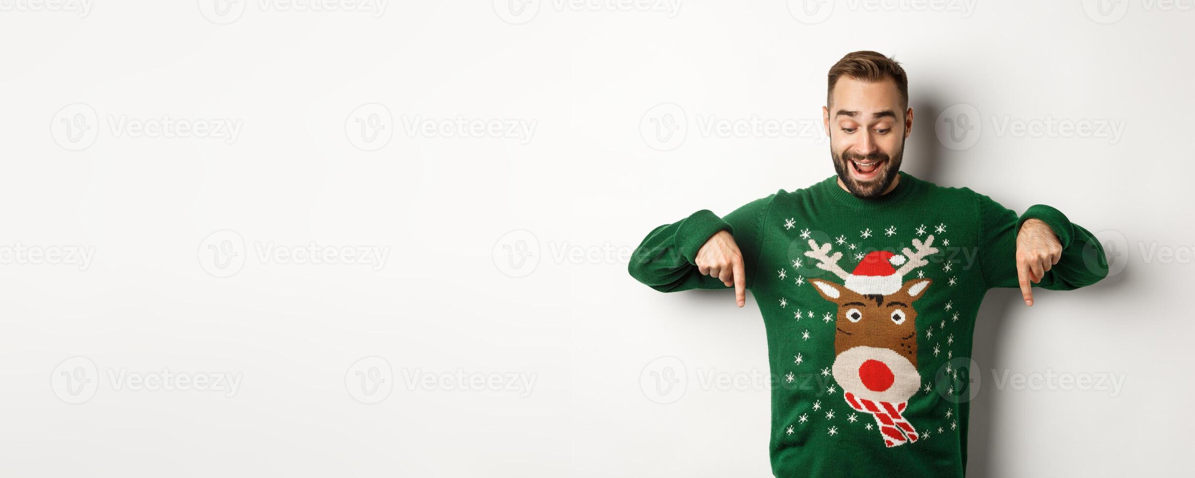 Winter holidays and christmas. Happy bearded man in green sweater, looking and pointing fingers down at advertisement, showing copy space, white background photo