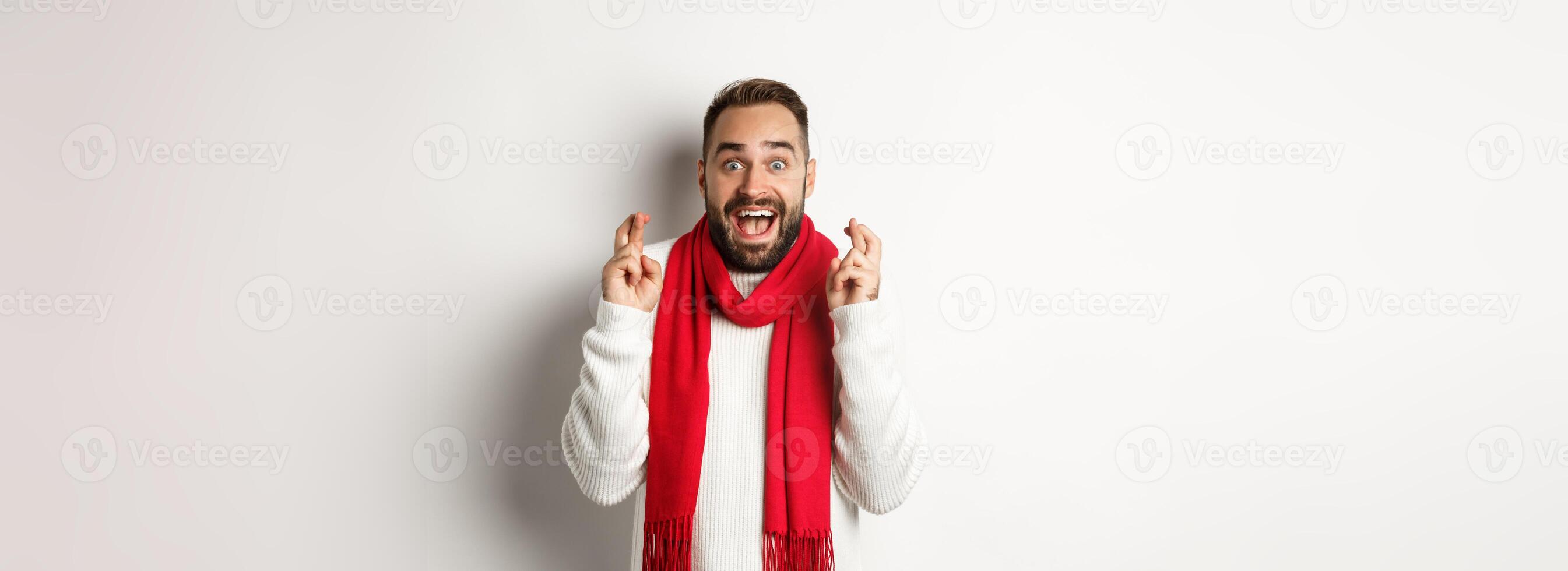 Christmas holidays and New Year concept. Hopeful man making wish with fingers crossed, waiting for gifts with excitement, standing over white background photo